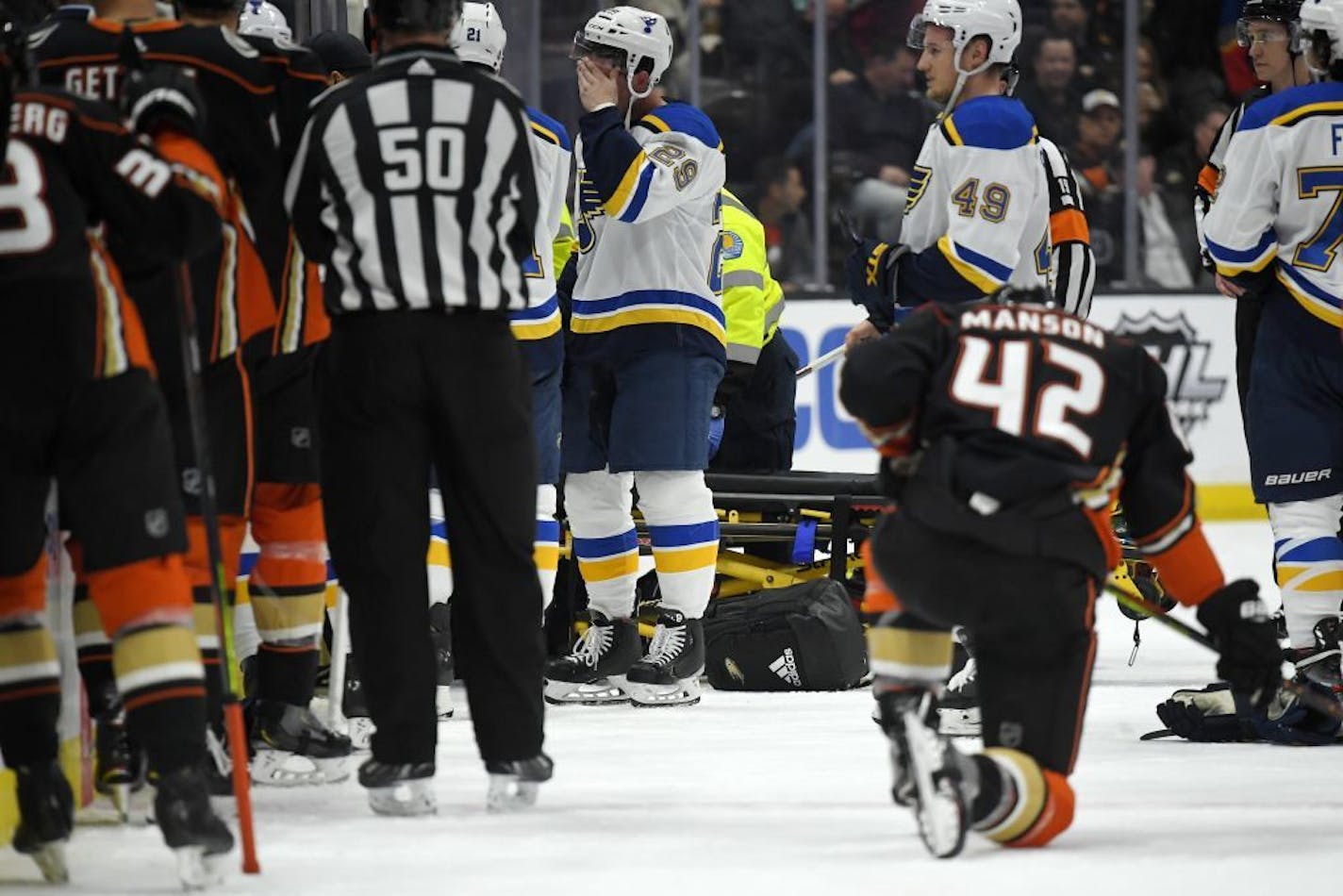 St. Louis Blues defenseman Vince Dunn, left, of center wipes his faces as Anaheim Ducks defenseman Josh Manson kneels on the ice while blues defenseman Jay Bouwmeester, who suffered a medical emergency, is worked on by medical personnel during the first period of an NHL hockey game Tuesday, Feb. 11, 2020, in Anaheim, Calif.