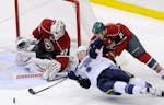 St. Louis Blues' T.J. Oshie reaches for the puck as he falls while giving chase around the net against Minnesota Wild's Kyle Brodziak (21) and goalie 