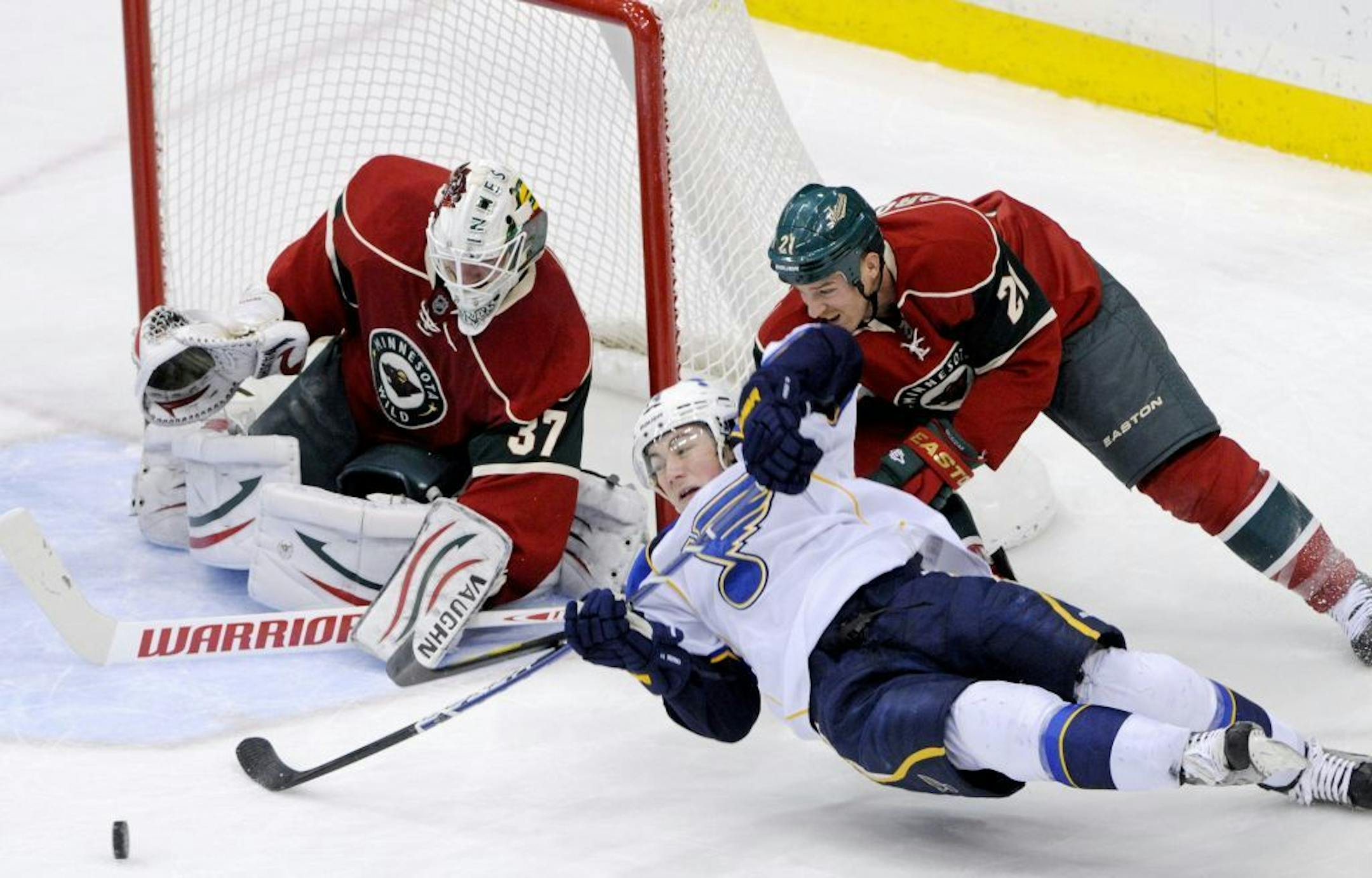 St. Louis Blues' T.J. Oshie reaches for the puck as he falls while giving chase around the net against Minnesota Wild's Kyle Brodziak (21) and goalie Josh Harding during the first period of an NHL hockey game, Saturday, Nov. 5, 2011, in St. Paul, Minn.