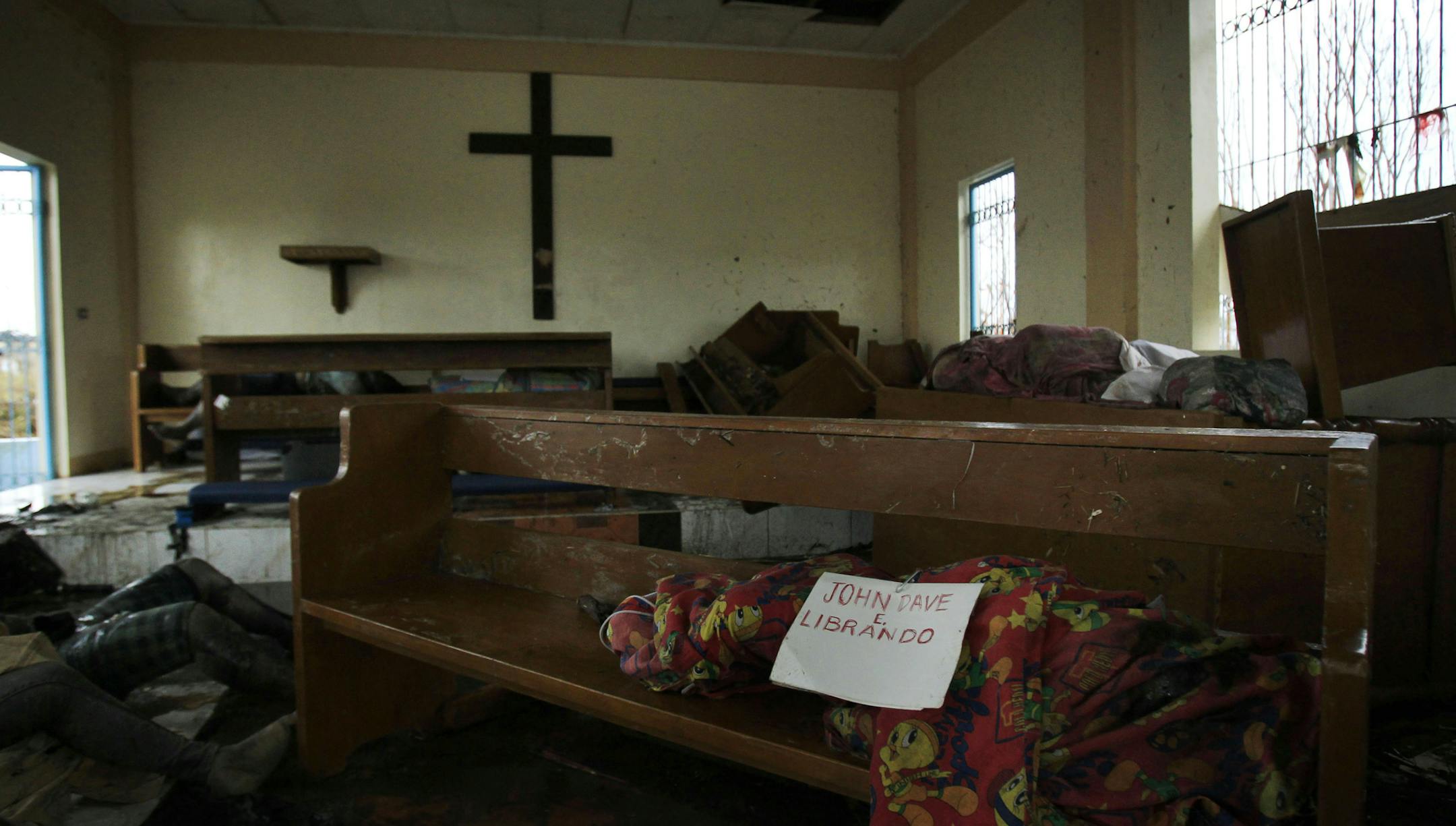 A body wrapped in cloth labeled only with a name is left on a pew at St. Michael The Archangel Chapel in Tacloban, central Philippines, Tuesday, Nov. 12, 2013. There is no functioning morgue here, so people have been collecting the dead from Typhoon Haiyan and storing them where they can ó in this case, St. Michael The Archangel Chapel. (AP Photo/Wally Santana)