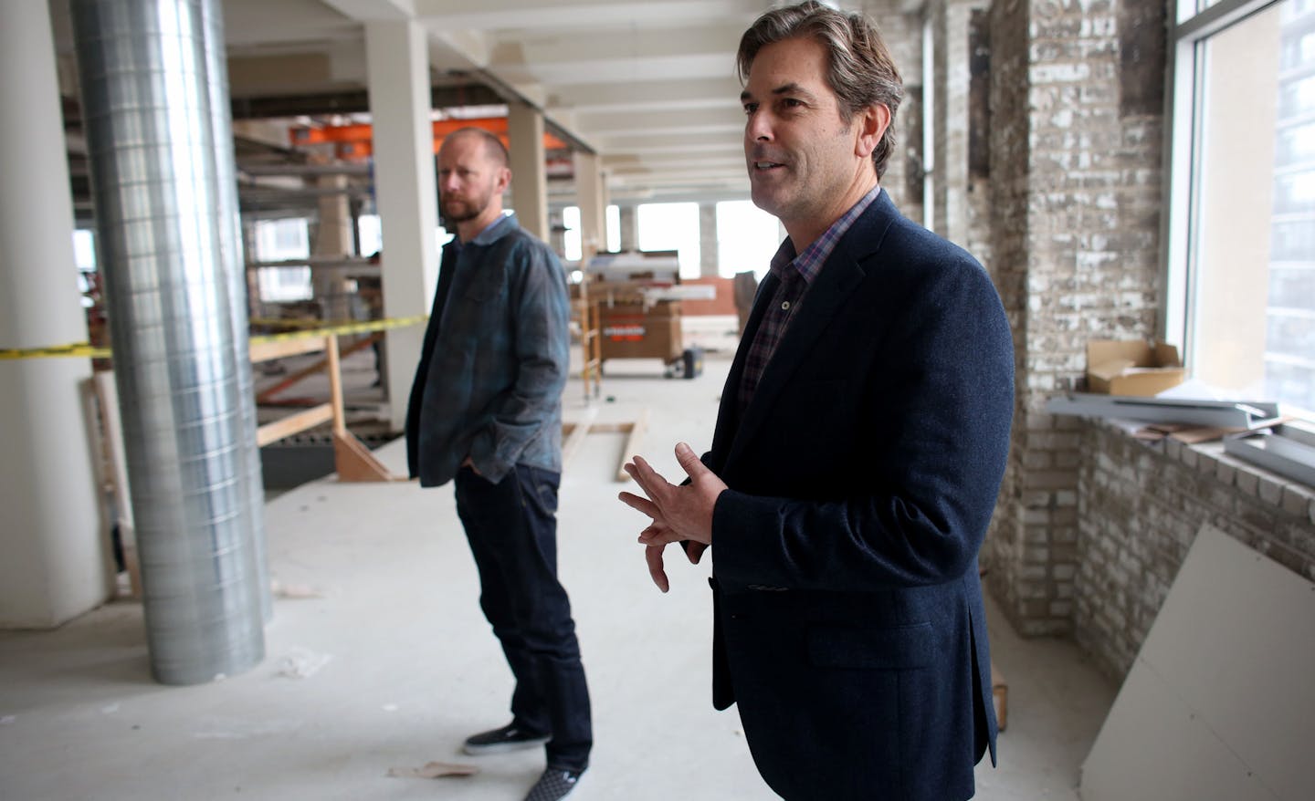 With David Carter, chief creative officer, behind him, Rob Buchner, chief executive officer at Mithun, talked about their new space and how they are keeping some of the elements of the original building but still have a modern minimalist feel. ] (KYNDELL HARKNESS/STAR TRIBUNE) kyndell.harkness@startribune.com At Mithun's new office space in Minneapolis , Min., Tuesday, November 11, 2014.