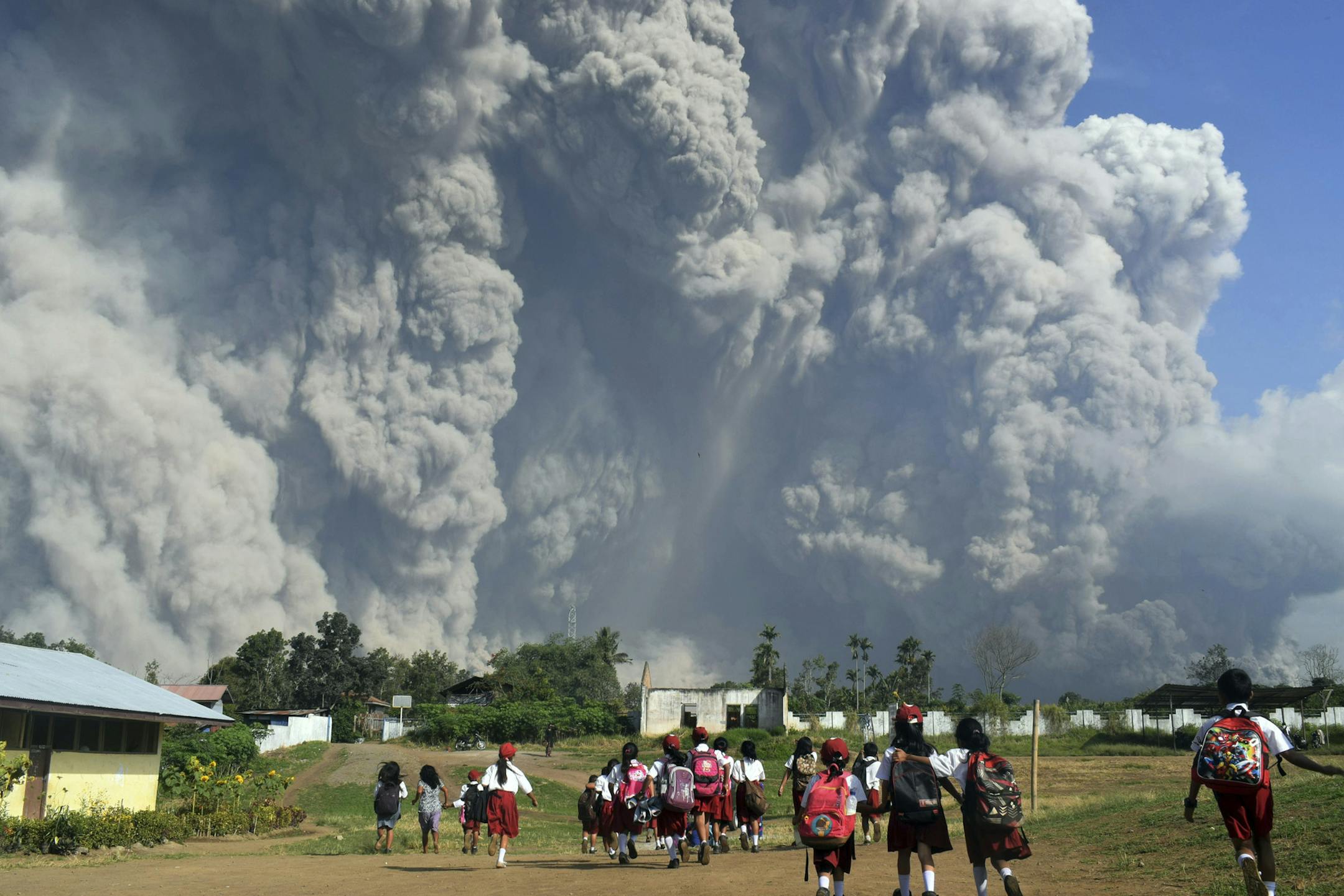 In this Monday, Feb. 19, 2018, file photo, school children walk as Mount Sinabung erupts in Karo, North Sumatra, Indonesia. Rumbling Mount Sinabung on the Indonesian island of Sumatra has shot billowing columns of ash more than 5,000 meters (16,400 feet) into the atmosphere and hot clouds down its slopes. The volcano, one of three currently erupting in Indonesia, was dormant for four centuries before exploding in 2010. (AP Photo/Sarianto, File)
