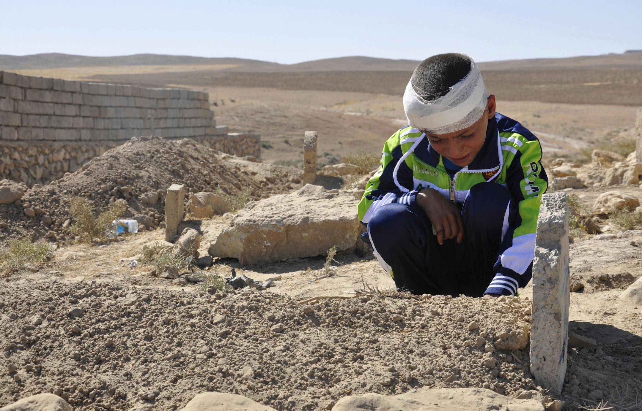 Mohammed Moses grieves by the grave of his father who was killed Sunday by a suicide car bomb attack near Qabak elementary school in the Shiite Turkomen village of Qabak, just outside the town of in Tal Afar, 260 miles (420 kilometers) northwest of Baghdad, Iraq, Monday, Oct. 7, 2013. Deadly attacks in Iraq killed tens of on Sunday, including a dozen children slain when a suicide bomber detonated the explosives-laden car he was driving near their elementary school in the north of the country, of