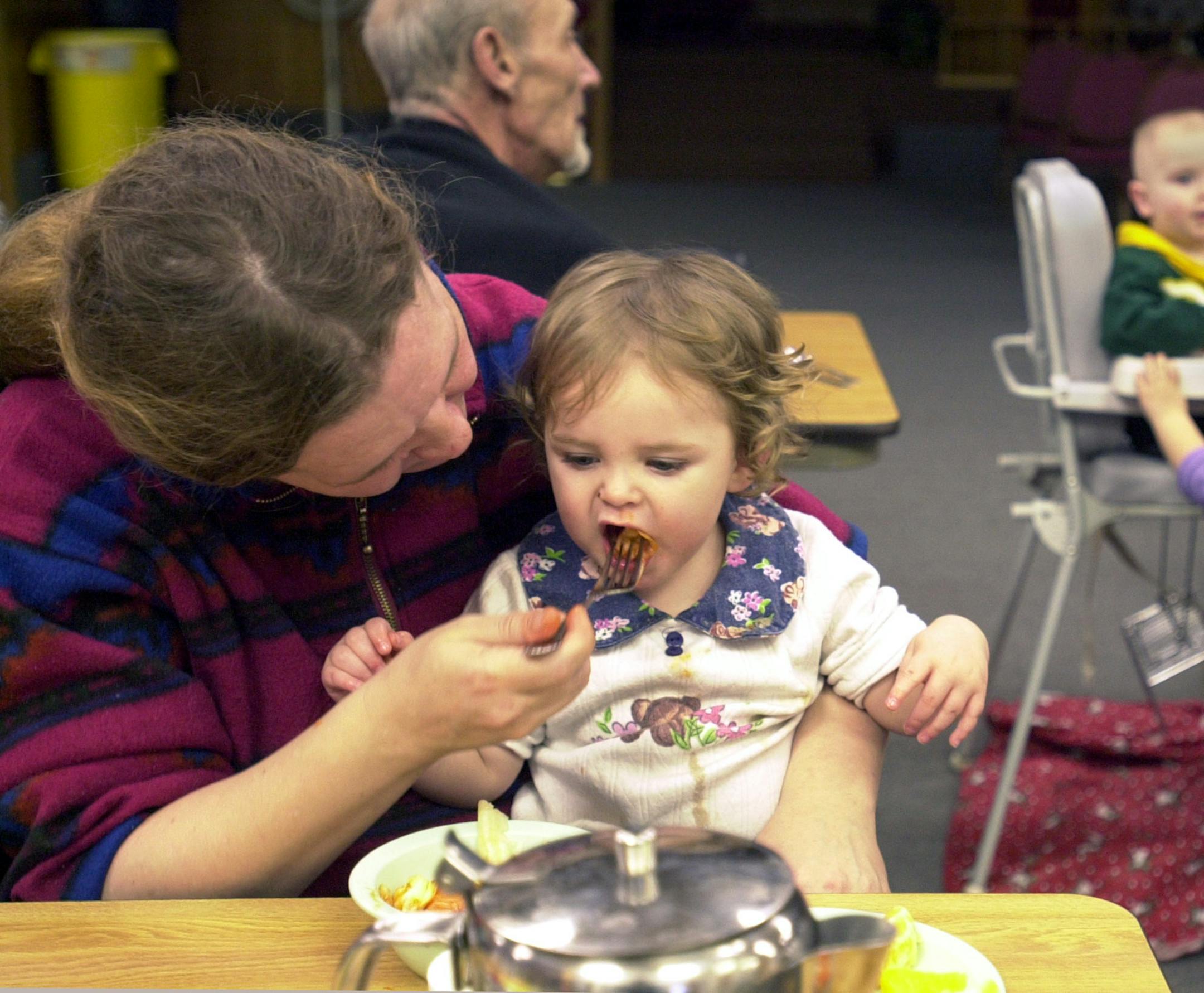 Hibbing, Mn., Weds., Mar. 5, 2003--(Left to right) Debbie Juntunen of Hibbing feeds her granddaughter, one-year-old Angel Wood, as her other granddaughter, two-year-old Mattie Wood, visits with a baby at the Hibbing Salvation Army Melting Pot Meals Program. Juntunen and her husband are trying to start a snow removal and lawn care business. After eating, Juntunen cleared and washed down the tables at the Salvation Army.
GENERAL INFORMATION: Iron Range food banks are seeing more first-time users d