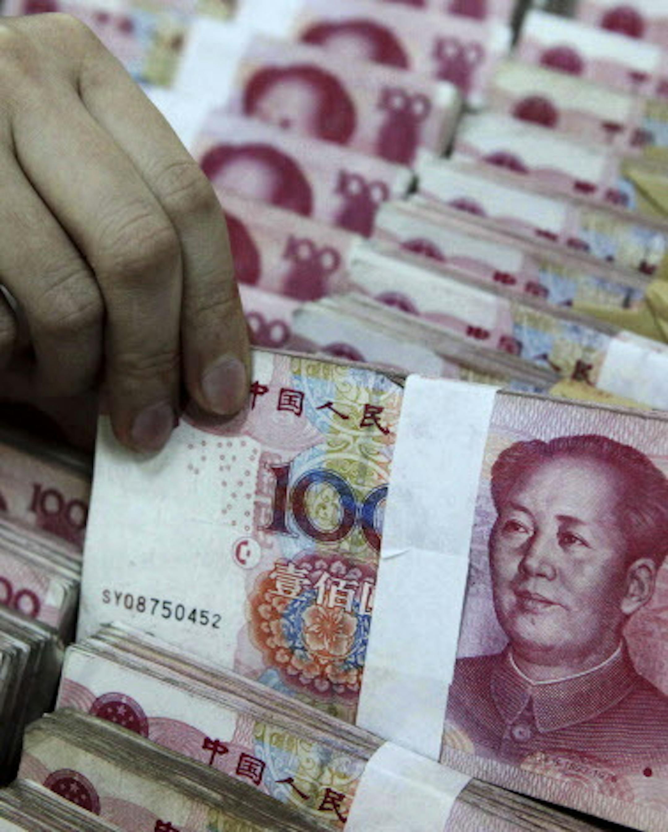 In this photo taken Tuesday, April 5, 2011, a clerk holds up a bundle of 100 yuan notes at a bank in Beijing, China. China's foreign reserves, by far the world's largest have surged past $3 trillion, driven by currency controls that Washington and other governments complain are distorting trade and hampering a global recovery. (AP Photo) CHINA OUT
