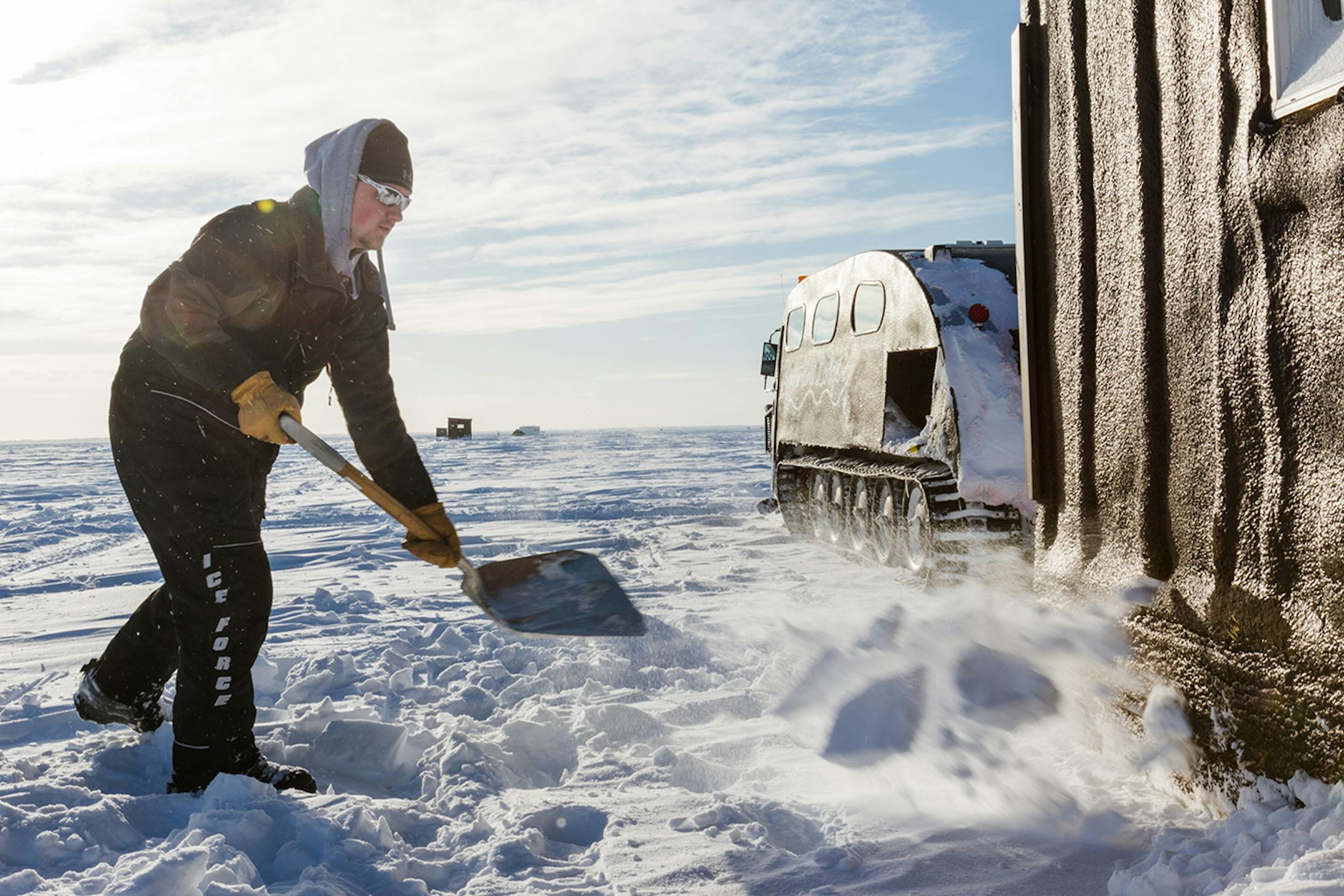 Baihly Hontvet shovels snow around the base of an ice house to insulate it from the cold.