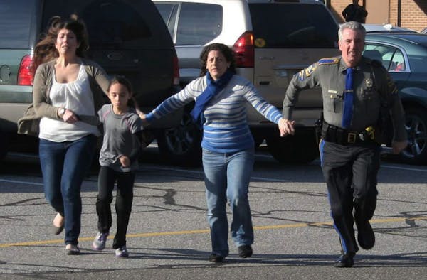 A police officer leads two women and a child from Sandy Hook Elementary School in Newtown, Conn., where a gunman opened fire, killing 26 people, inclu