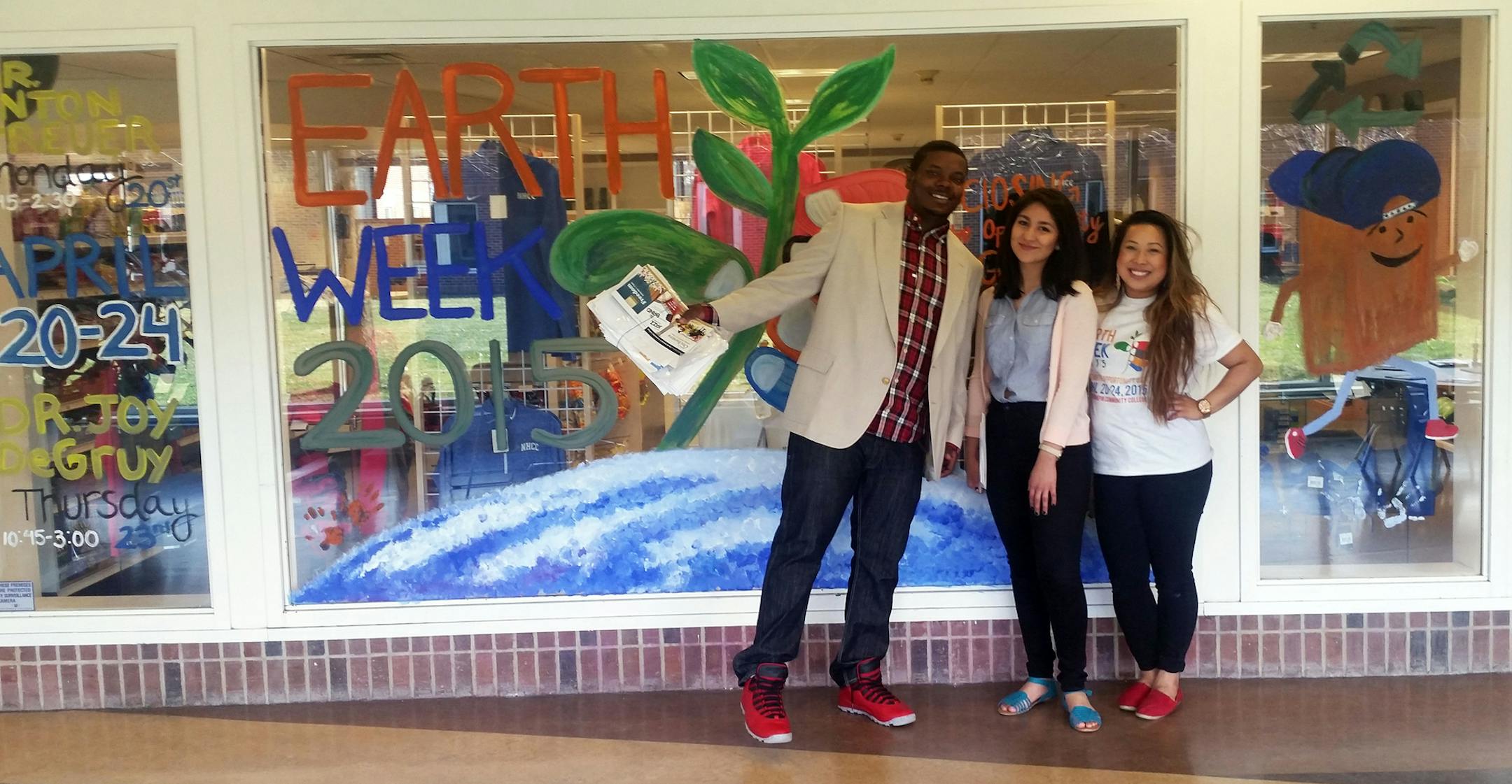 Sonny Holden, Jocelyn Hernandez and Kimber Pathoumthong stand in front of a sign for Earth Week at North Hennepin Community College. The three are classmates in the community organizing class that is putting on the event.