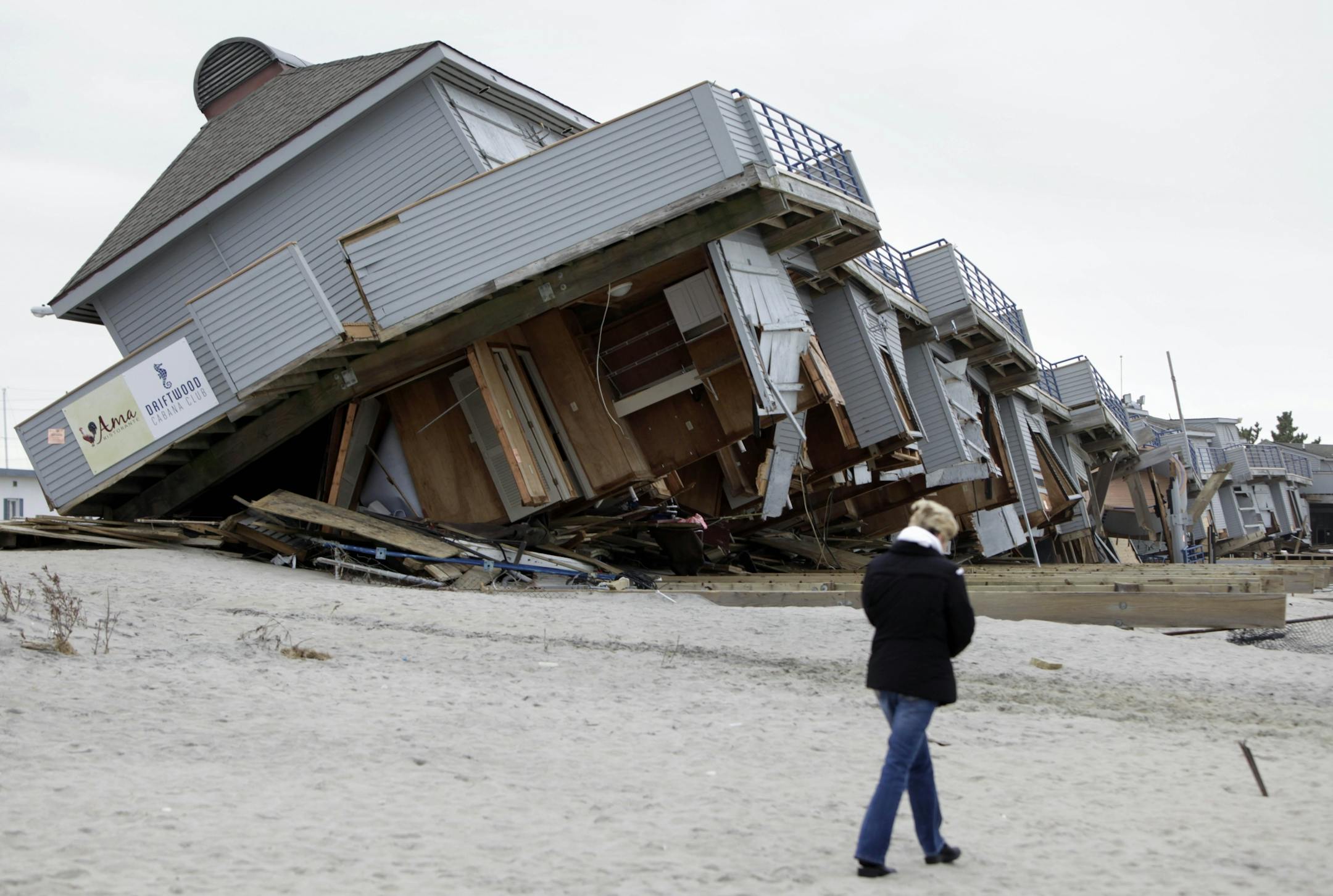 A woman walks past a cabana complex on the beach pulled off its foundations by Superstorm Sandy in Sea Bright, N.J., Monday, Nov. 19, 2012.