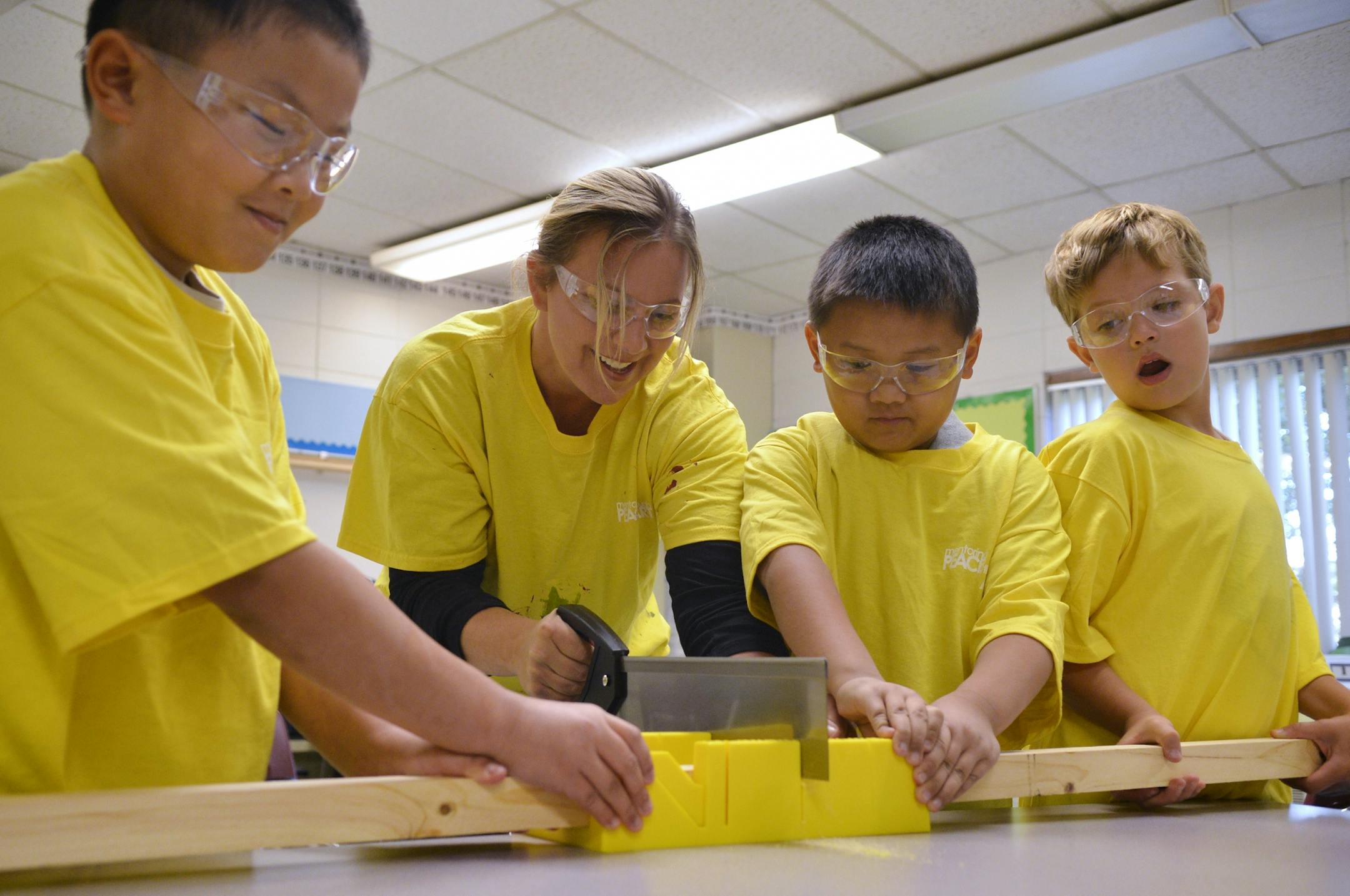 Evergreen Park World Cultures Community School third grade teacher, Nikki Erickson (center left) saws lumber to create the frame for a mural project while her students, Safety Team members (from left) Anthony Lee, Avan Thao, and Aaron Endris hold the wood in place.