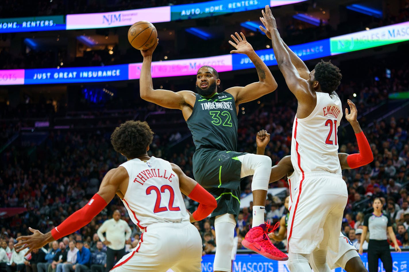 The Timberwolves' Karl-Anthony Towns, center, passes the ball while Philadelphia 76ers' Joel Embiid, right, defends the basket during the first half Saturday