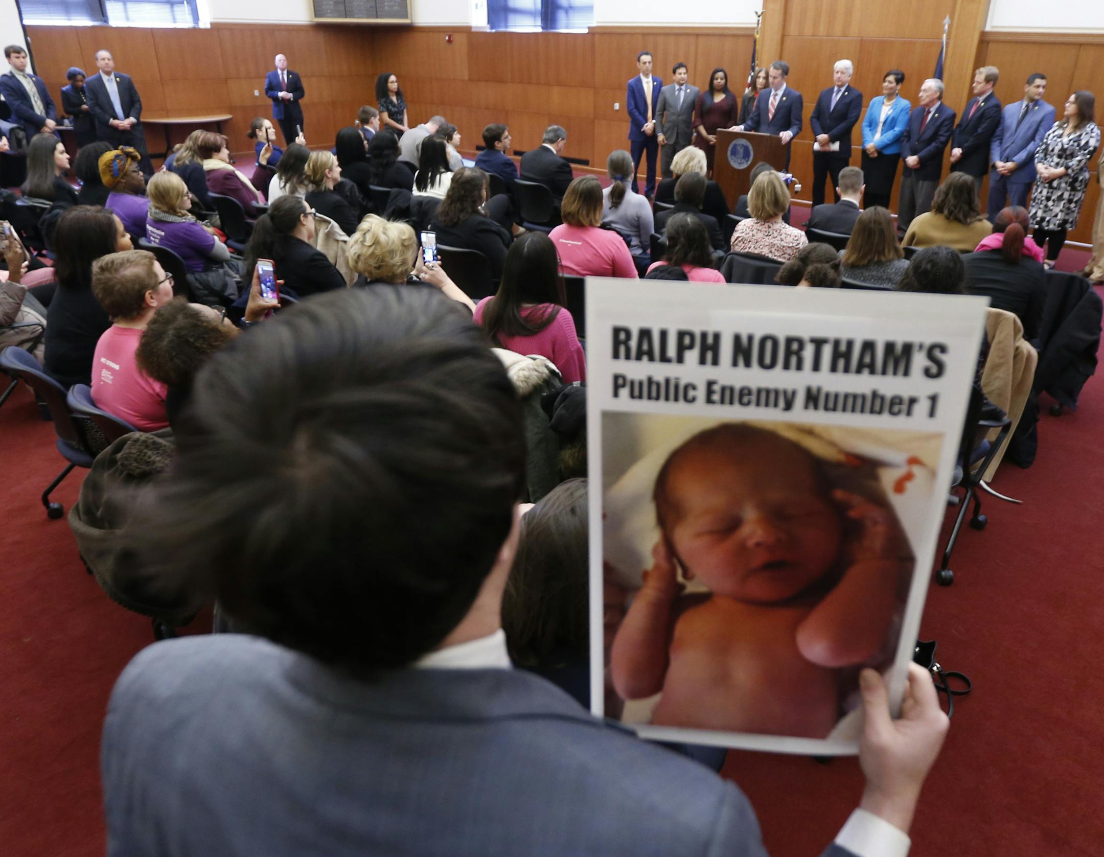 A demonstrator holds a sign as Gov. Ralph Northam, at podium, gives a news conference at the Capitol in Richmond, Va., Thursday, Jan. 31, 2019. Northam made a statement and answered questions about the late term abortion bill that was killed in committee. (AP Photo/Steve Helber)