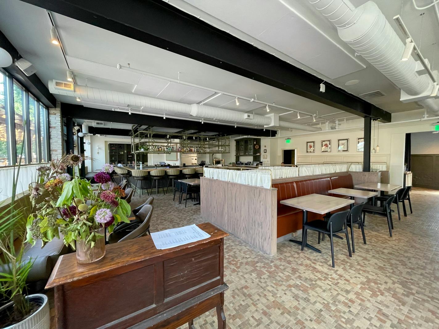 The open dining room with white ceiling and cream walls is broken up by a few tables and a vintage desk hostess stand.