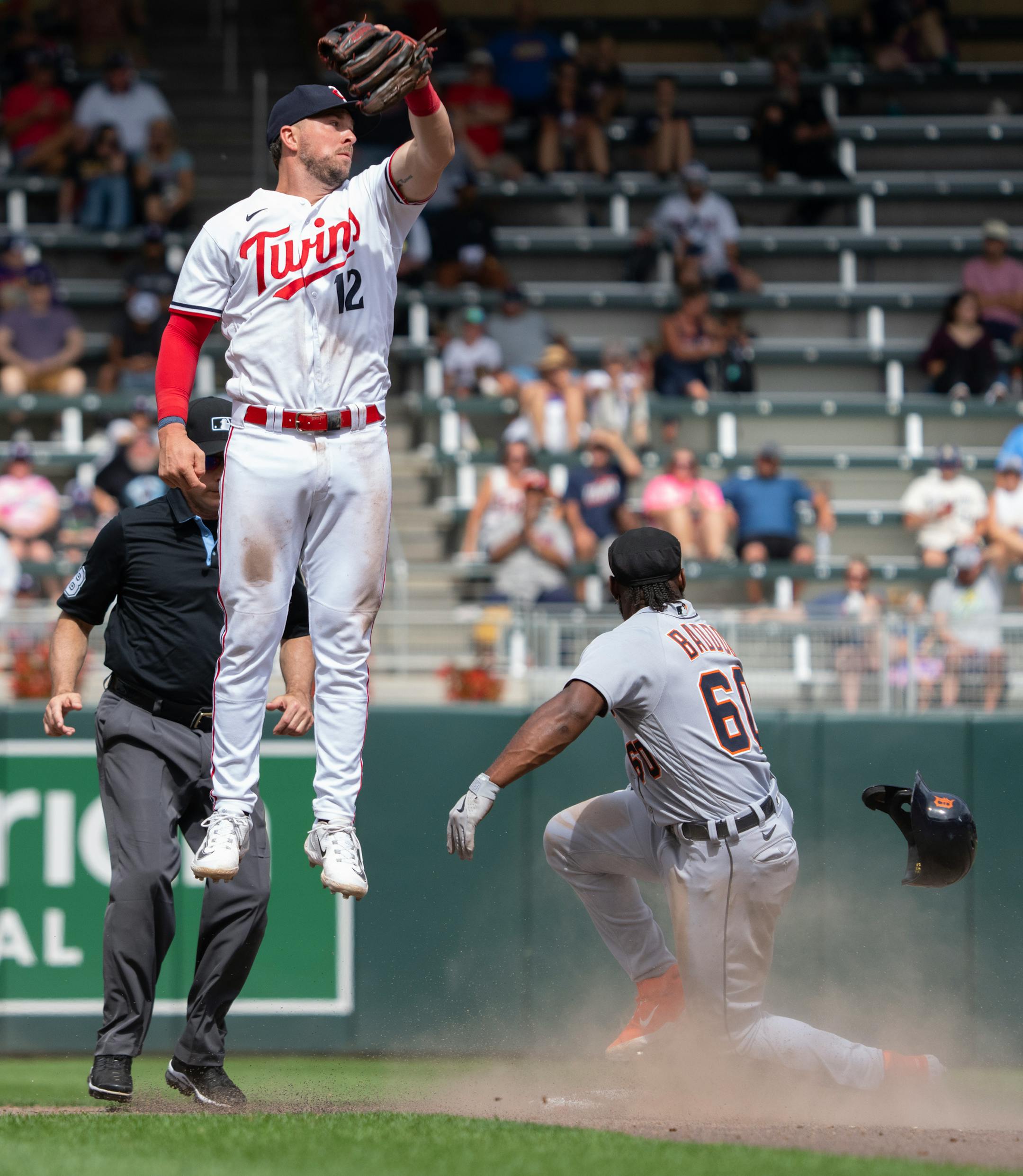 Minnesota Twins shortstop Kyle Farmer (12) jumps high to try and catch an errant throw as Detroit Tigers left fielder Akil Baddoo (60) steals second base in the ninth inning.