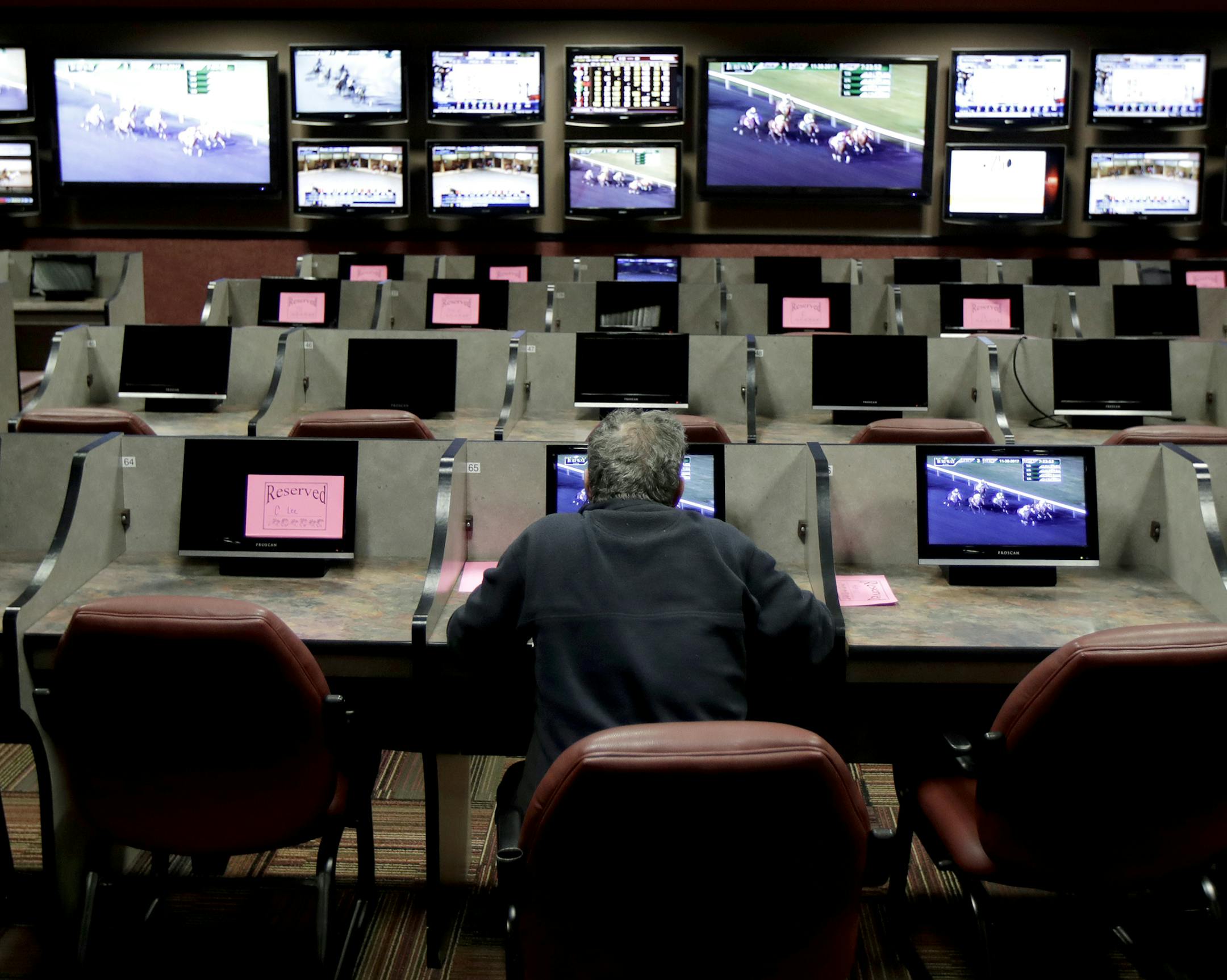 In this Nov. 30, 2017, photo, a man sits at a cubicle watching a simulcast horse race at the Monmouth Park racetrack in West Long Branch, N.J. With banks of TVs tuned to all-sports stations and a spacious bar, the lounge a the racetrack is a sports gamblers’ paradise-in-waiting. All that’s standing in its way: A 25-year-old federal law that bars betting on sports in most states. The high court is weighing On Dec. 4, whether a federal law that prevents states from authorizing sports