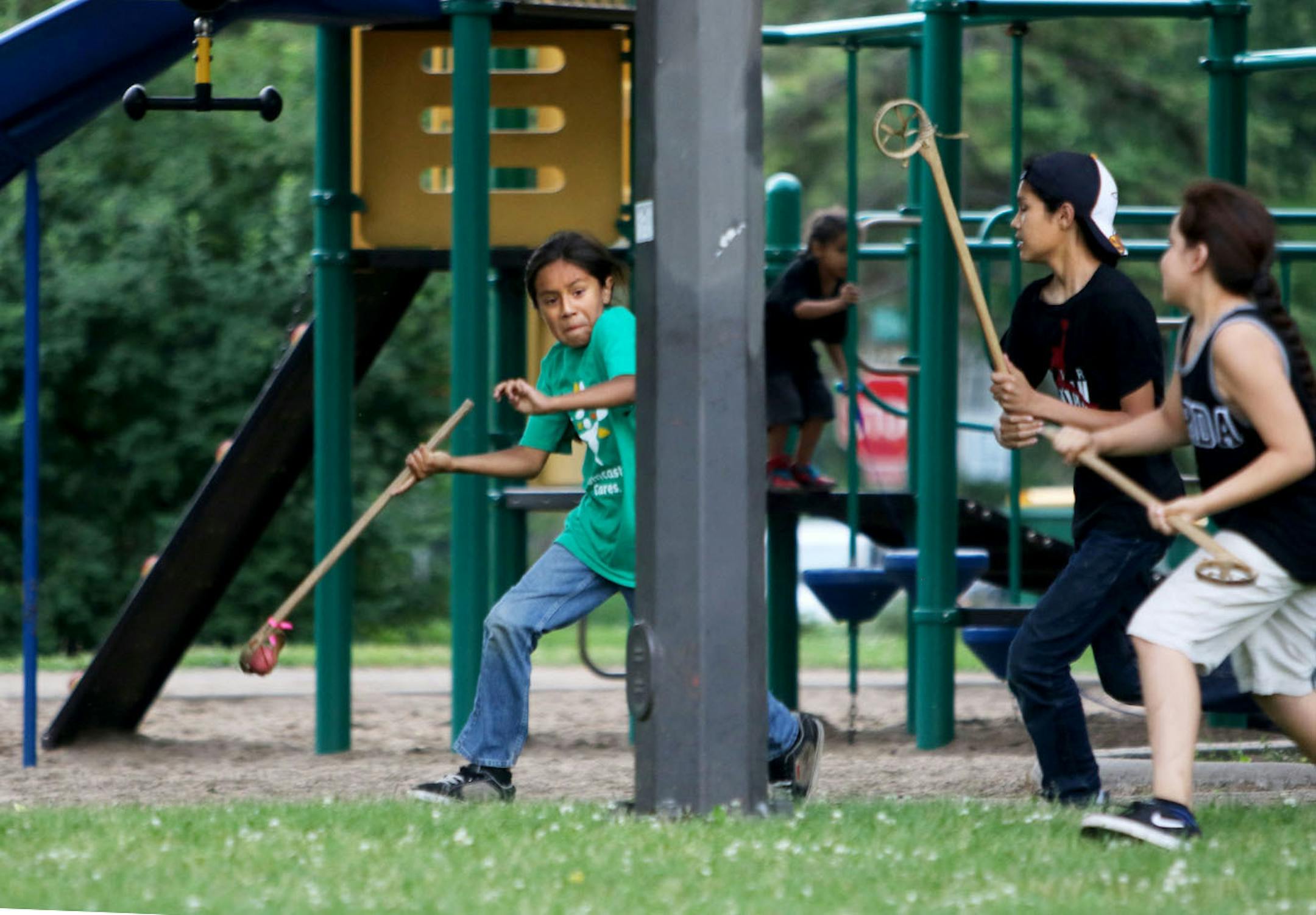Youth members of Twin Cities Native Lacrosse practice at Corcoran Park Wednesday, June 17, 2015, in Minneapolis, MN. The traditional Lacrosse players, who play with hand carved ash sticks, were preparing for the upcoming Twin Cities Native Lacrosse Tournament at the Osseo High School Saturday. Here, Santino DeCory, left to right, tries to elude defenders Bronson Grant and Mato Ska Thompson, after the ball rolled underneath playground equipment and play continued.