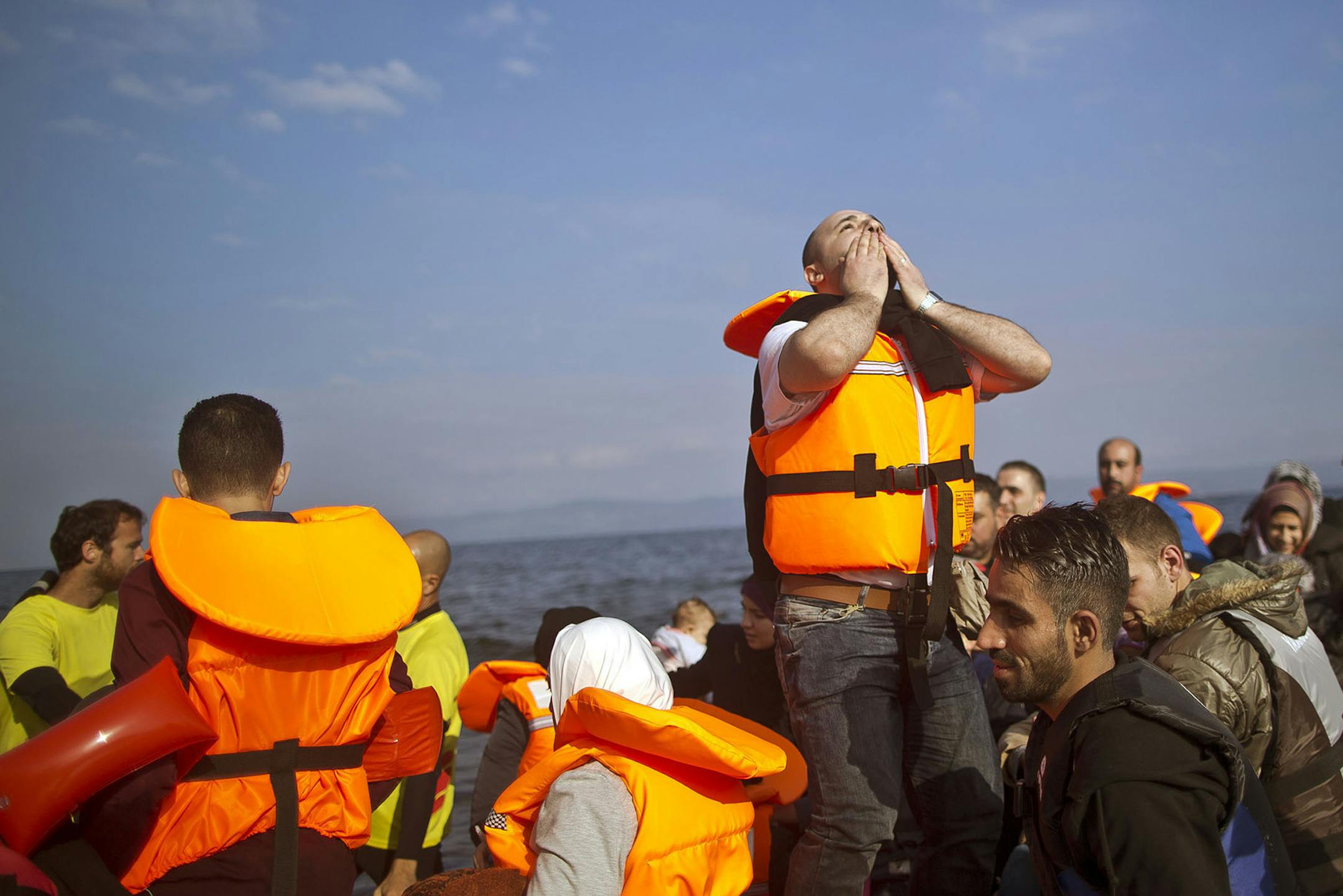 FILE - In this Saturday, Oct. 3, 2015 file photo, Syrian refugee Mahmoud Naoura, 30, center, chants "Thanks God we are safe,"while standing on a dinghy arriving from the Turkish coast to the northeastern Greek island of Lesbos. Bold ideas for helping Syrian refugees and their overburdened Middle Eastern host countries are gaining traction among international donors who were shocked into action by this year's migration of hundreds of thousands of desperate Syrians to Europe. (AP Photo/Muhammed Mu