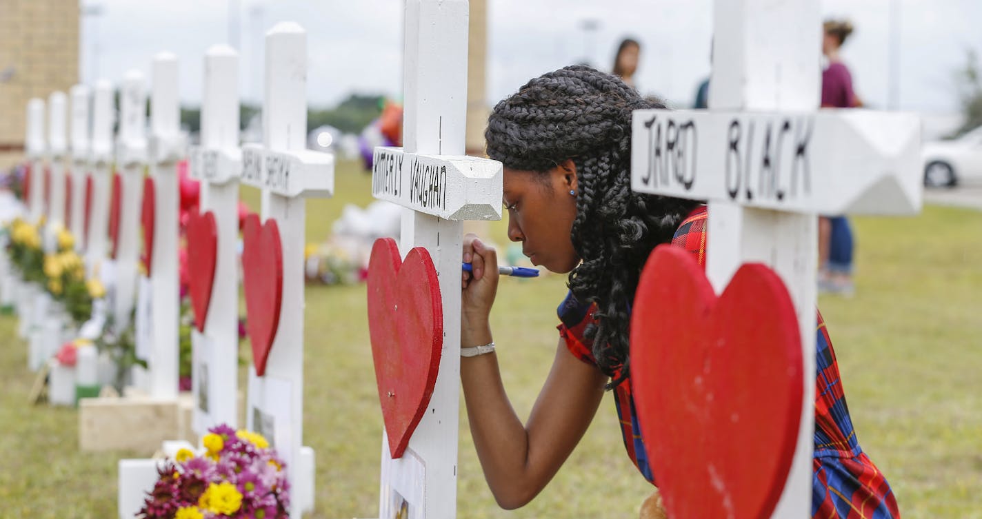 Santa Fe High School freshman, Jai Gillard writes messages on each of the 10 crosses in front the school Monday, May 21, 2018, in Santa Fe. Gillard, was in the art class Friday morning, knew all of the victims of the shooting. Texas Governor Greg Abbott has called for a moment of silence at 10 a.m. and came to the school to participate. (Steve Gonzales/Houston Chronicle via AP)