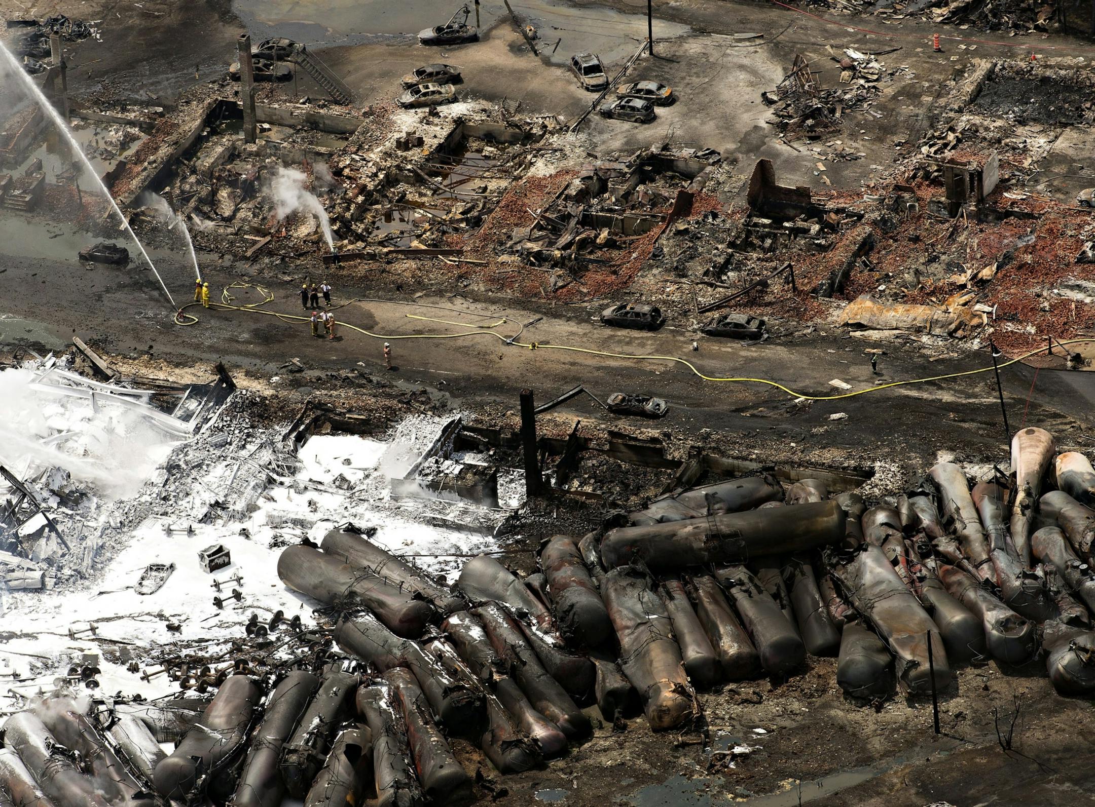 The downtown core lays in ruins as fire fighters continue to water smoldering rubble Sunday, July 7, 2013 in Lac Megantic, Quebec. A runaway train derailed Saturday igniting tanker cars carrying crude oil.