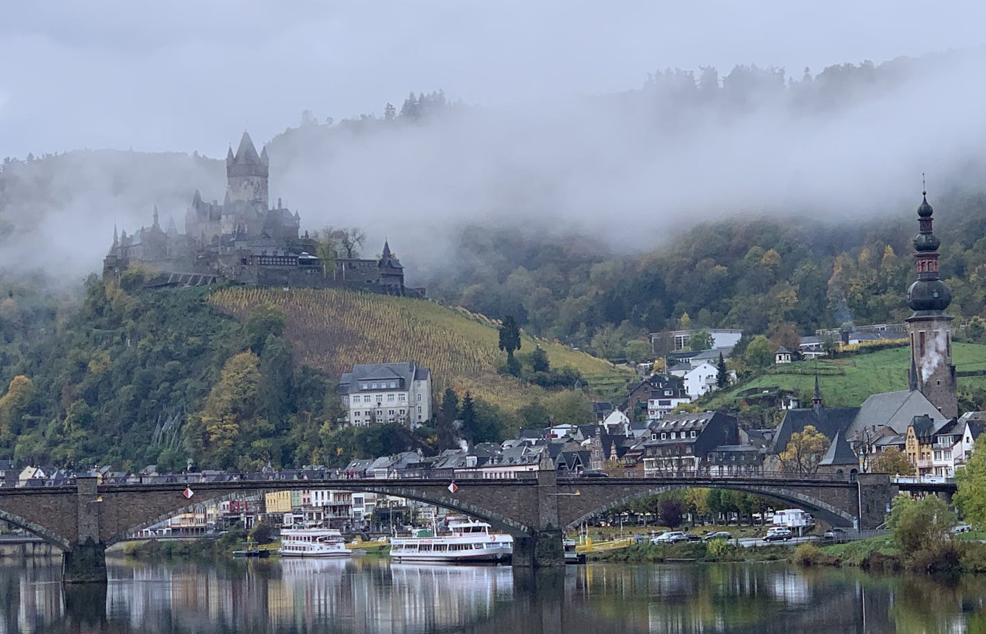 I will try to provide the information you are seeking. My name is Sheldon "Sam" Sampson and I live in Faribault, Minnesota.
I was on a Viking river cruise with my wife and we docked in Cochem, Germany on the Mosel River
This photo shows a calm river and the castle Reichsburg which overlooks the city along the river with morning fog. It is among the larger castles on the Mosel.
I took this photo with my Apple iPhone XS at 8:57 am on November 3, 2019 from the top deck of the cruise ship while it w