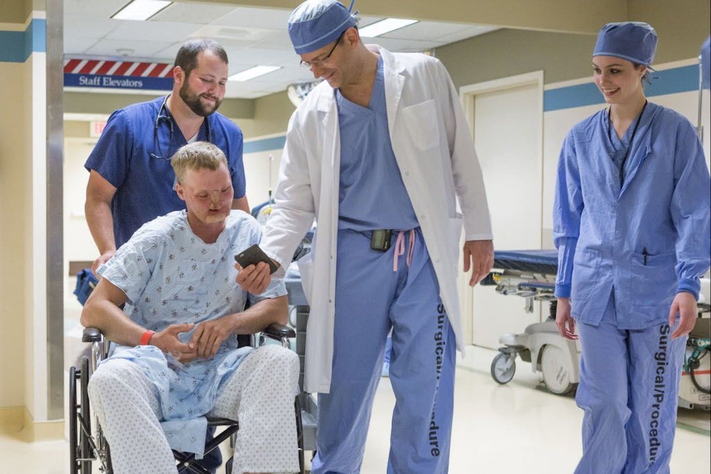 In this June 10, 2016 photo provided by the Mayo Clinic, Dr. Samir Mardini shows Andy Sandness photos of his children on his smartphone before Sandness' face transplant surgery in Rochester, Minn. Over the years, the two say they've become as close as brothers.