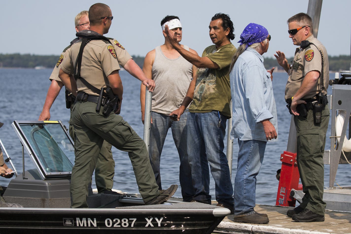 Jim Northrup (center in green shirt) Todd Thompson (left with white headband) and Leonard Thompson (right with blue headband) talk with conservation officers at a public dock after having their nets siezed from Gull Lake. ] Northrup and Thompson were chased off the lake and given citations by state conservation officers who then pulled the 200-foot long net from the water and carried it away. Brian.Peterson@startribune.com Nisswa, MN - 8/27/2015