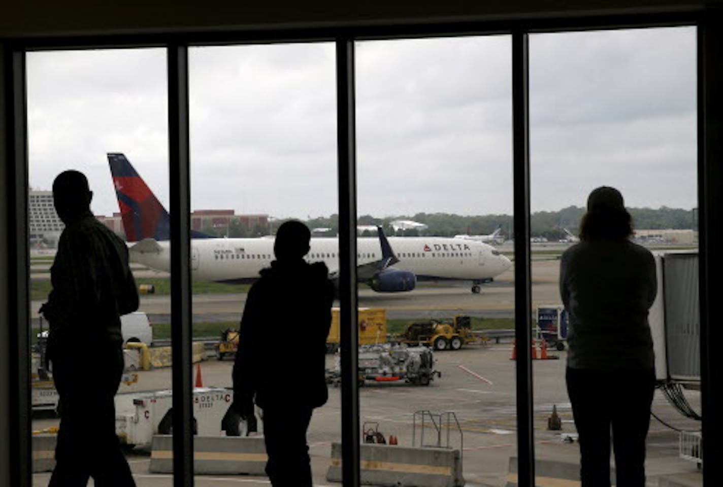 In this photo taken Tuesday, April 14, 2015, Delta Airlines passengers watch as a Delta plane taxis at Atlanta's Hartsfield International Airport in Atlanta. Delta Air Lines said Wednesday, April 15 that the strong dollar is hurting ticket sales in some foreign markets and announced plans to pull back international service, primarily in Japan, Brazil, India, Africa and the Middle East. (AP Photo/Charles Rex Arbogast)