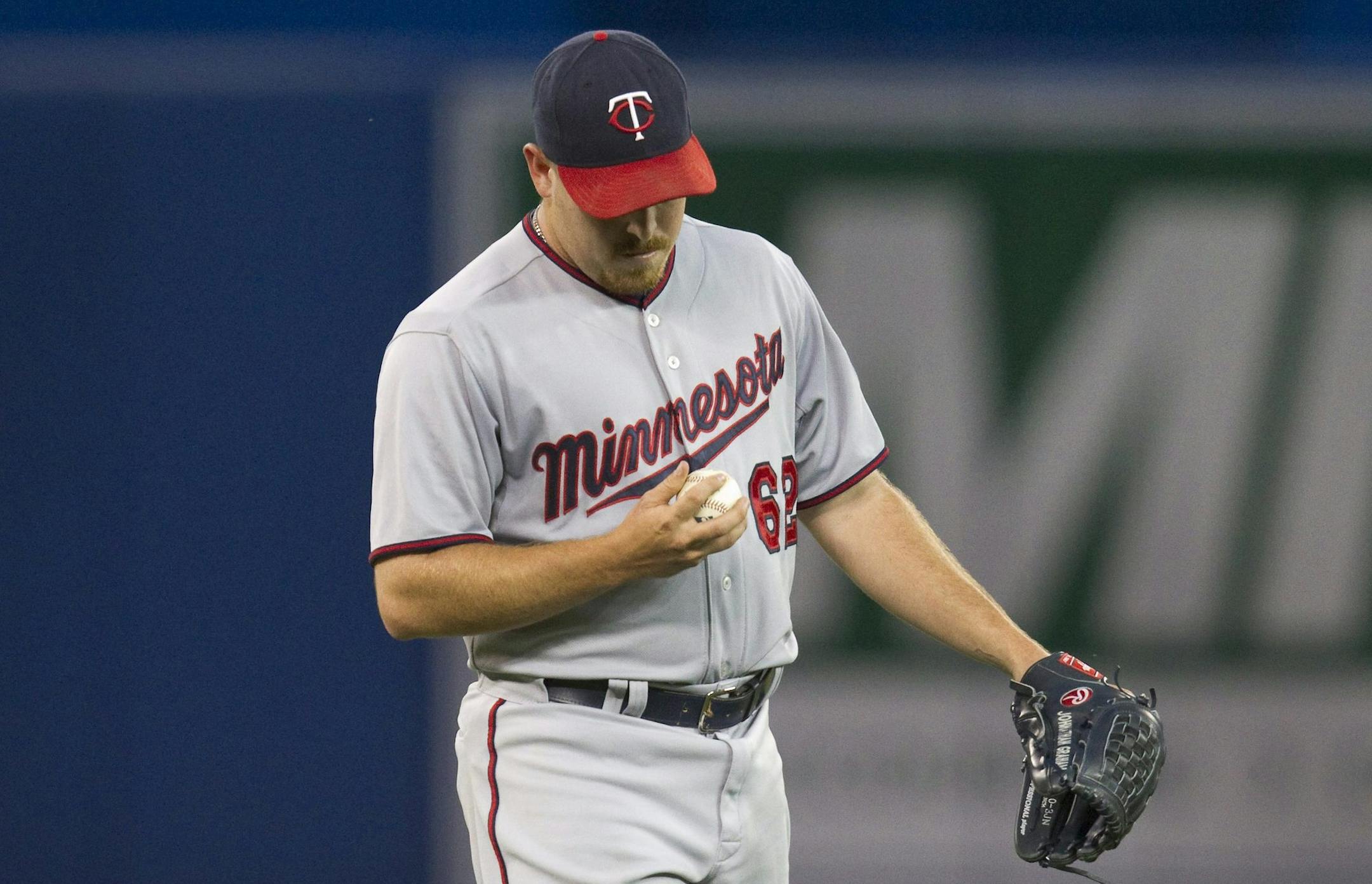 Minnesota Twins pitcher J.R. Graham pauses to look at the baseball after he gave up a three-run home run to Toronto Blue Jays' Edwin Encarnacion during the fourth inning of a baseball game Wednesday, Aug. 5, 2015, in Toronto. (Fred Thornhill/The Canadian Press via AP)