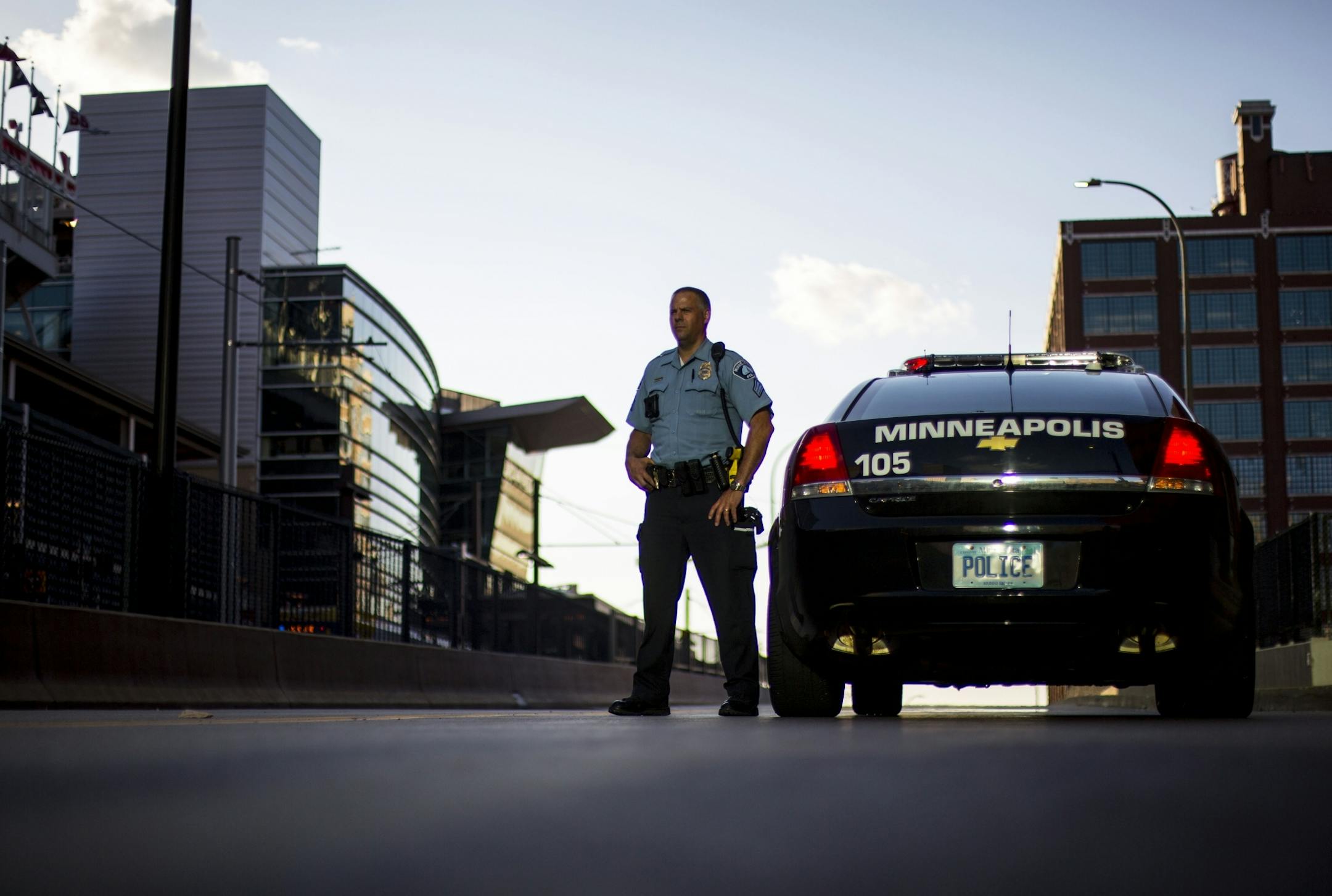 A police officer watches the protestors in front of Target field as he stands next to his car.
