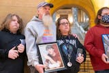 Jason Lange holds a photo of his stepson, Travis Gustavson, while putting his arm around his wife and Travis' mother, Kim Gustavson, at an event calling for increased legislative action regarding fentanyl Tuesday, Feb. 21, 2023 at the Minnesota State Capitol in St. Paul. ]