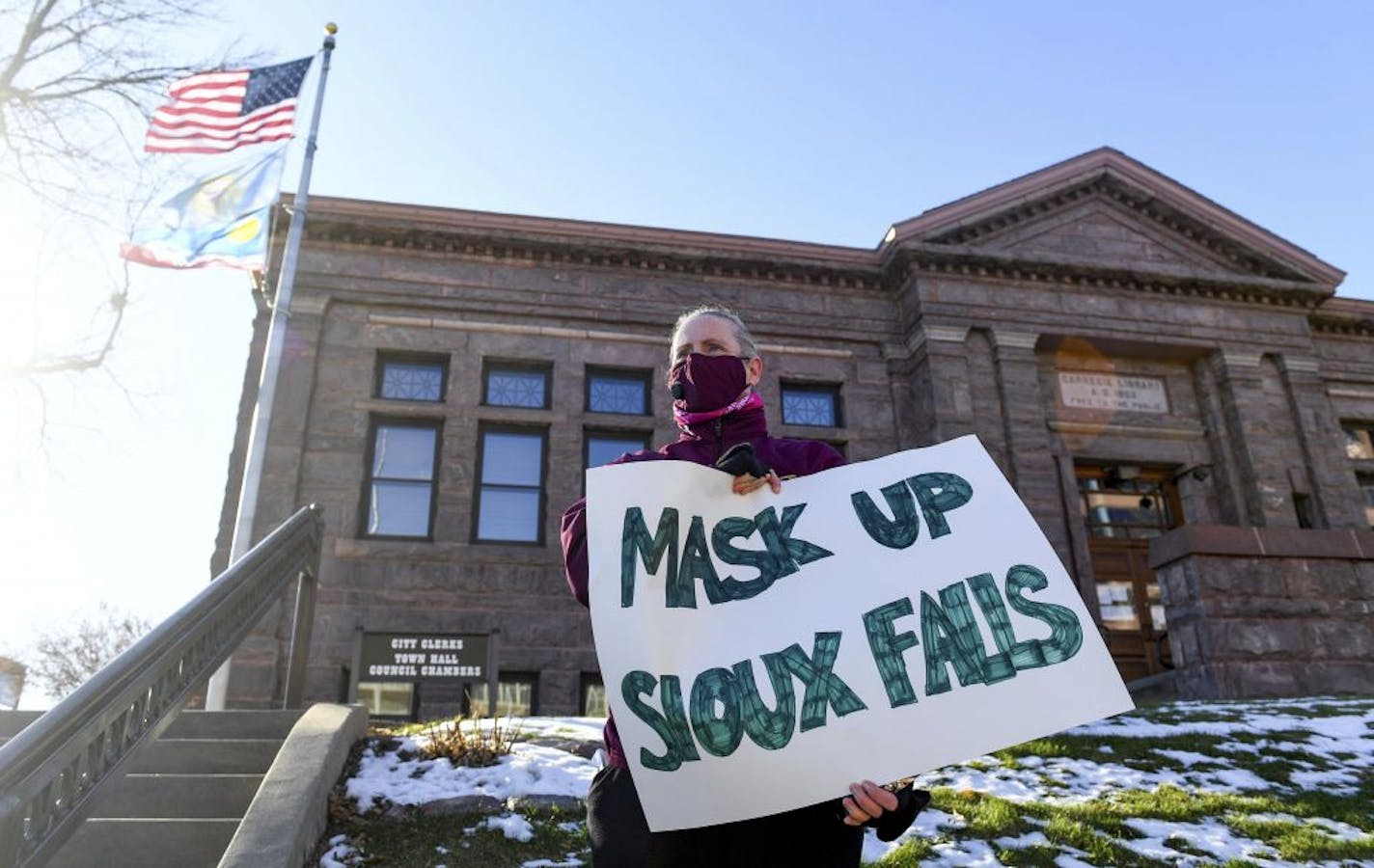 Jenae Ruesink holds a sign demanding a mask mandate from city council on Monday, Nov. 16, 2020 outside Carnegie Town Hall in Sioux Falls, S.D.