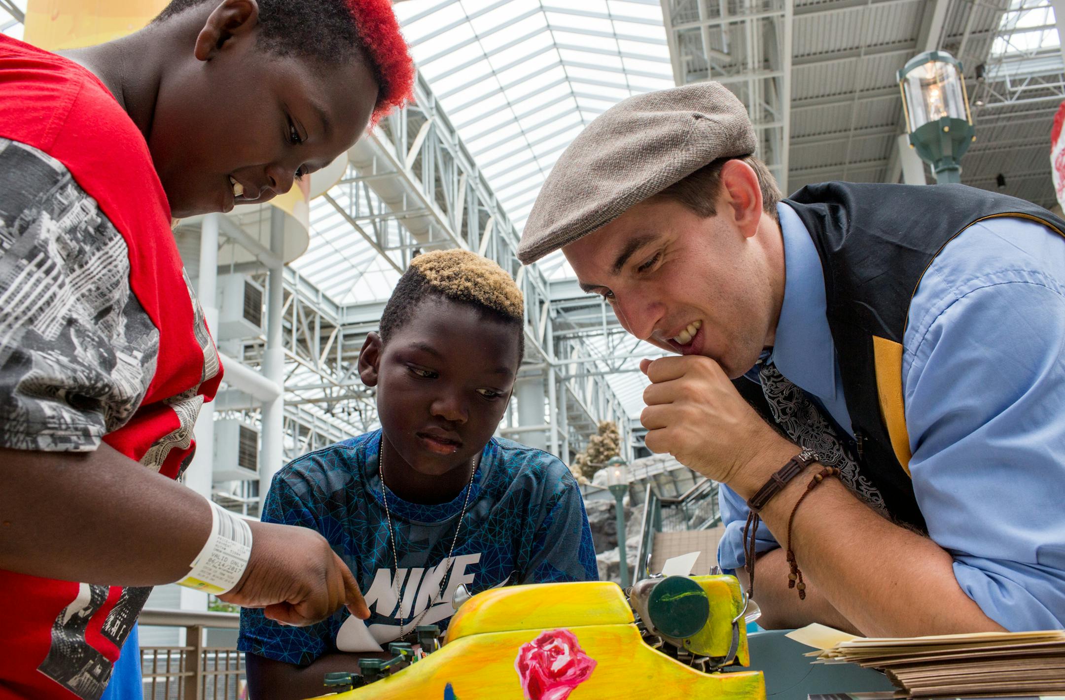 Brian Sonia-Wallace (right) shows Thomas (left) and Treyvion Starnes what a typewriter is and how to use it at the Mall of America. Sonia-Wallace uses a typewriter to write poetry for strangers he meets in the mall. ] COURTNEY PEDROZA &#x2022; courtney.pedroza@startribune.com June 14, 2017 Bloomington; Brian Sonia-Wallace writes poetry for strangers who walk up to him in the Mall of America