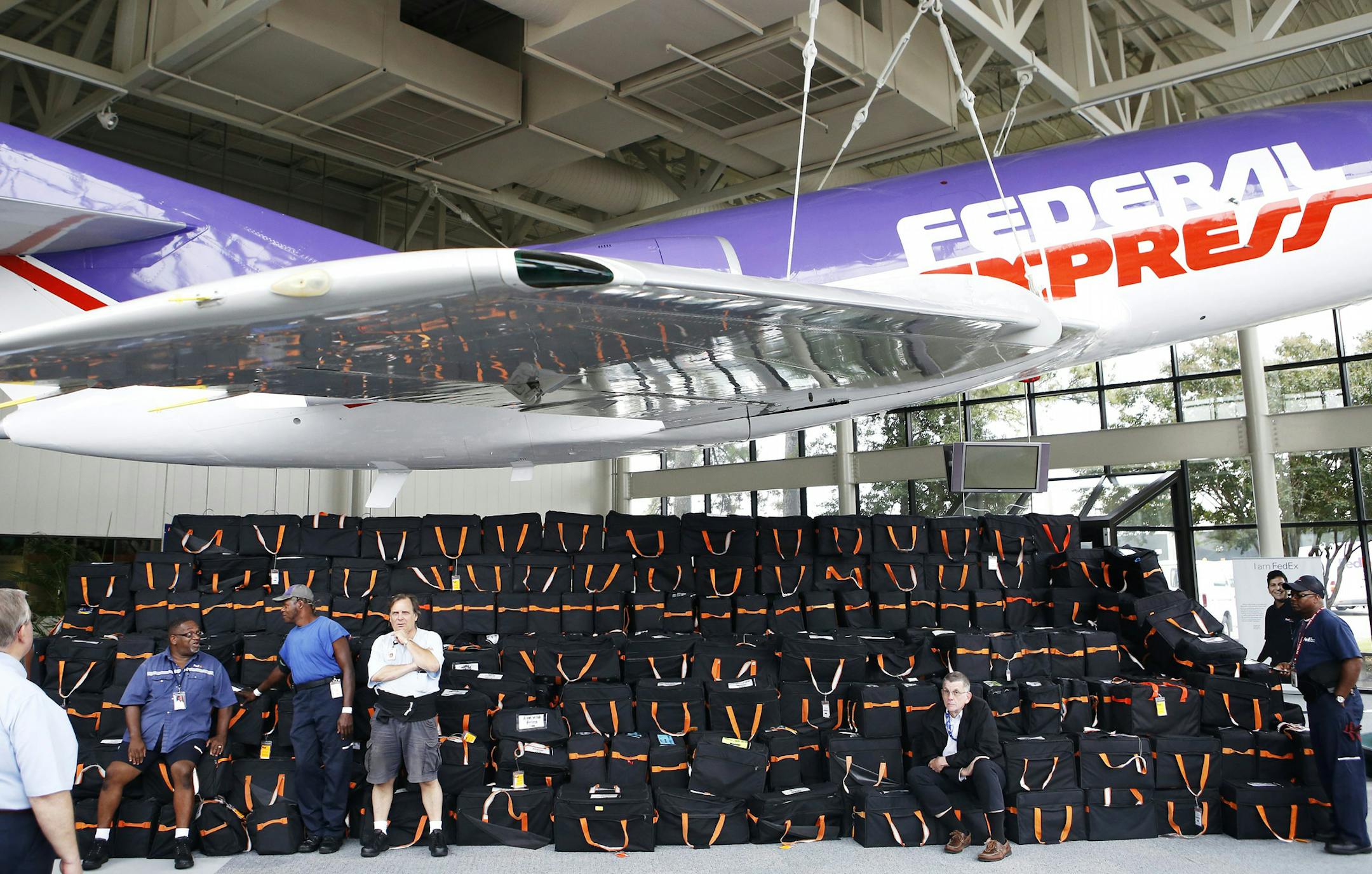 FedEx employees mingle around a large collection of flight bags containing pilot manuals placed underneath a Falcon Aircraft inside of the Greenway Building on Monday, Sept. 30, 2013 in Memphis, Tenn. FedEx is replacing all of the old flight bags, with a combined weight of 32 tons, with iPads that will digitally store the information that used to be in the paper manuals. (AP Photo/The Commercial Appeal, Brad Vest) ORG XMIT: MIN2013110120115381