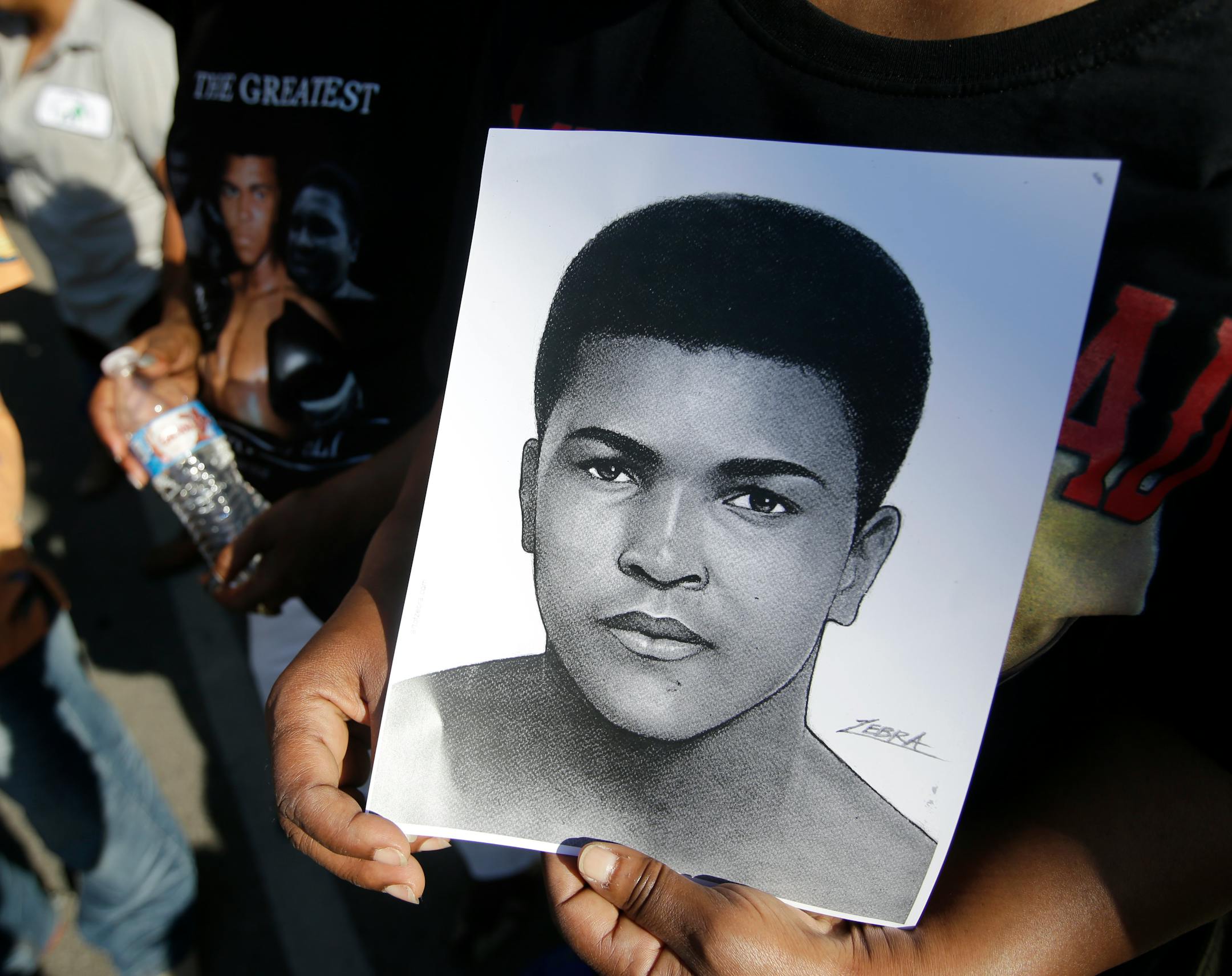 A mourner holds a photo of Muhammad Ali, as she waits for the procession to pass with the hearse carrying the body of Muhammad Ali, Friday, June 10, 2016, in Louisville, Ky. (AP Photo/Darron Cummings)