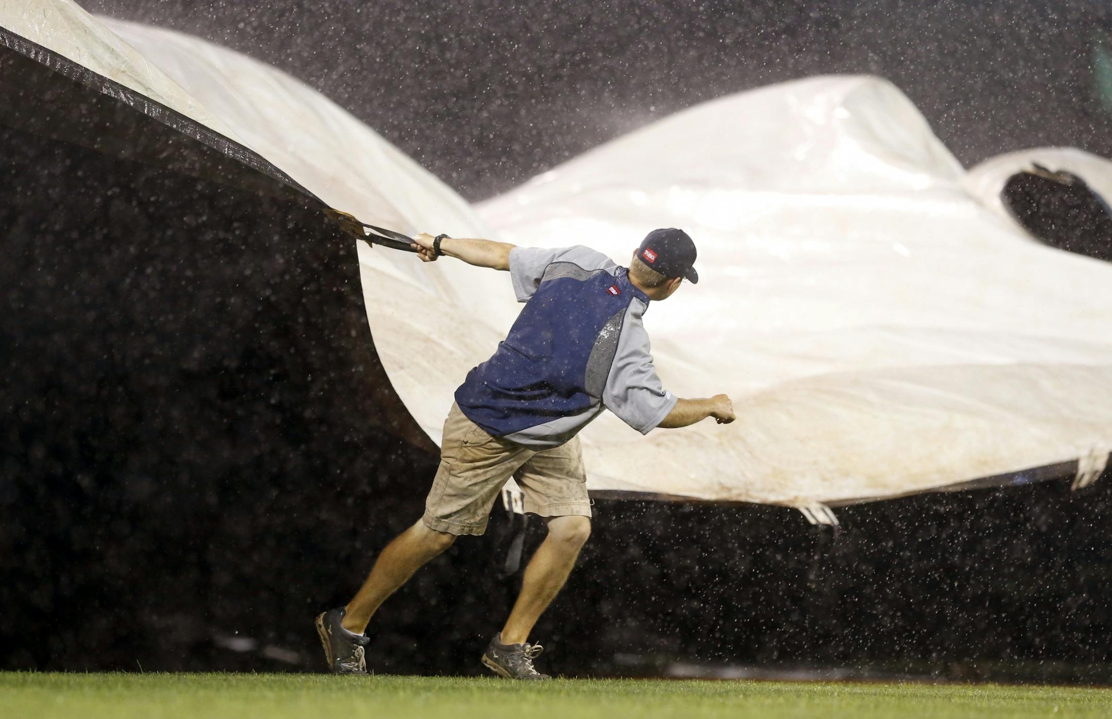 A Minnesota Twins grounds crew worker pulls the wind-blown tarp over the infield during a rain delay in the third inning of a baseball game against the Detroit Tigers Wednesday, Sept. 21, 2016, in Minneapolis.