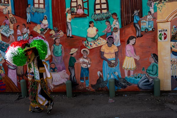 A member of Carnavaleros de Puebla made his way to the rest of the group past a large mural during an annual Cinco de Mayo celebration on Lake Street.