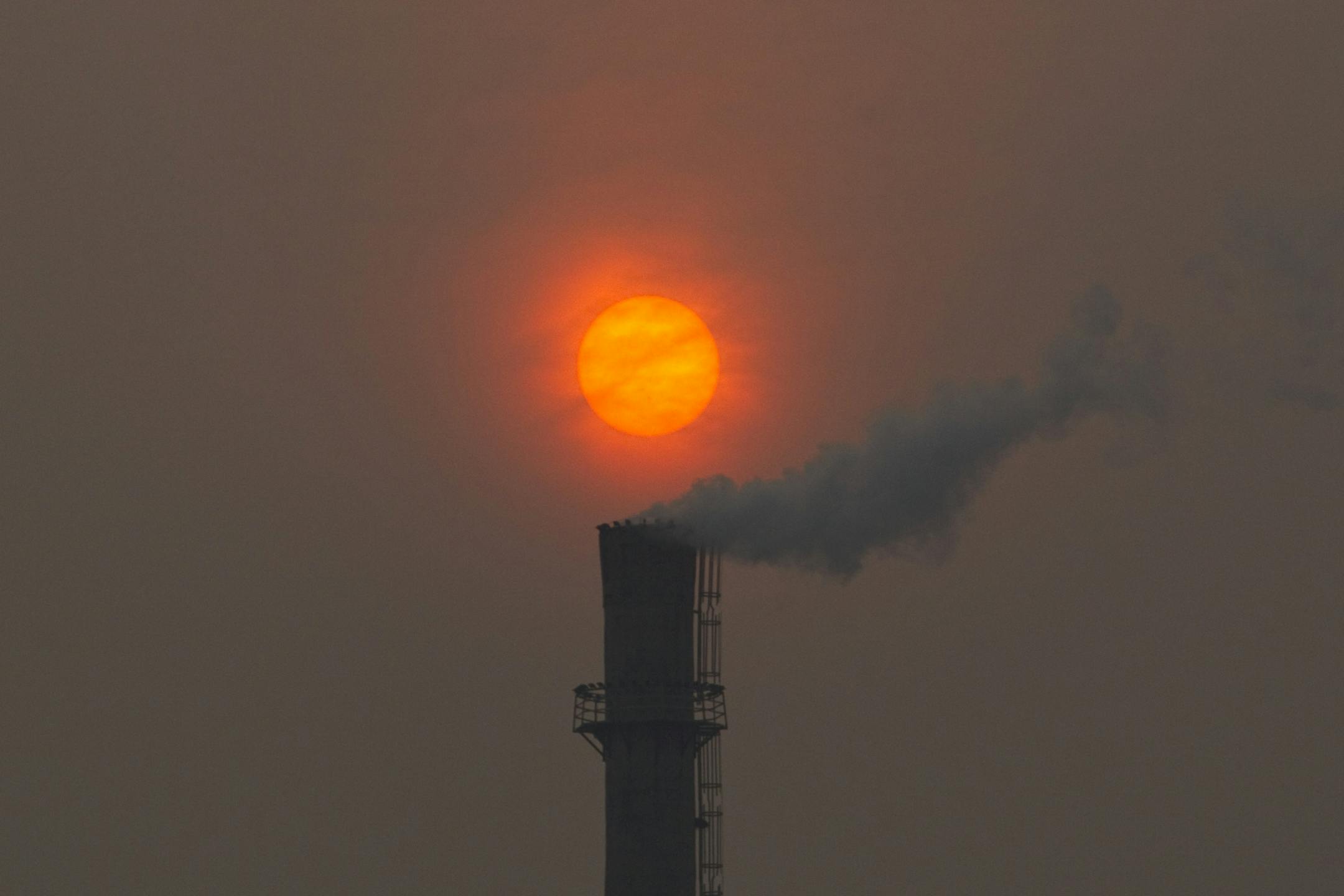 Smoke billows from a chimney of a heating plant as the sun sets in Beijing.