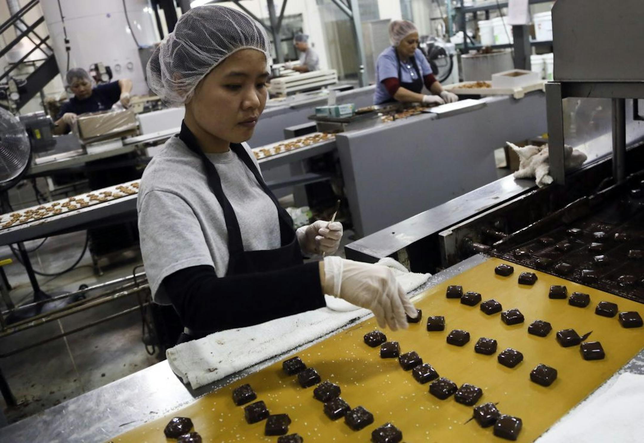 Candy maker Kim Heng sprinkles sea salt on top of dark chocolate covered cream caramel at Abdallah Candies in Burnsville, MN.