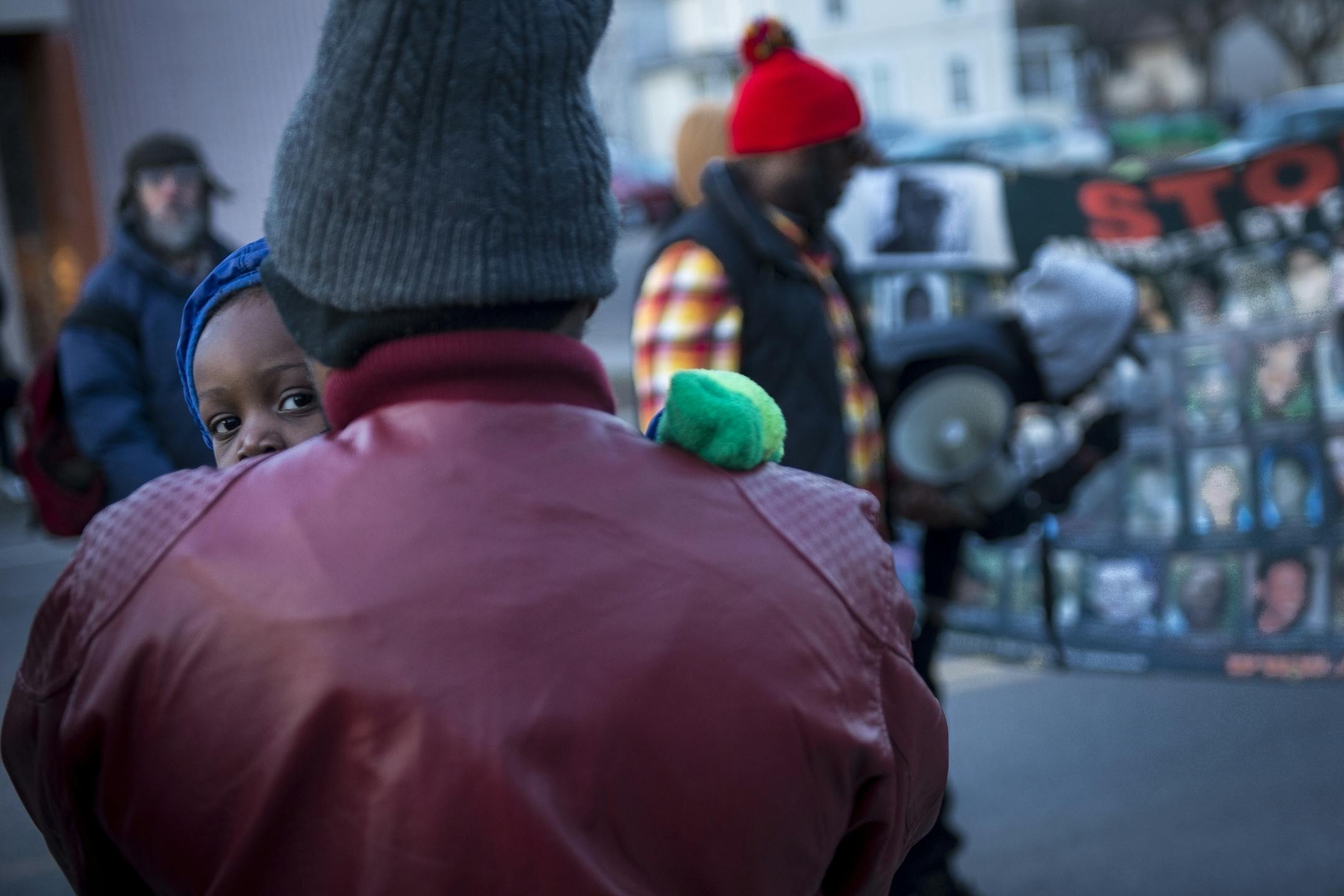 Lavance Dixon, of North Minneapolis, held his 2-year old son, Lucus, as organizers read the names of men, women and children killed by police off a poster Friday afternoon during a vigil at Jamar Clark's memorial.