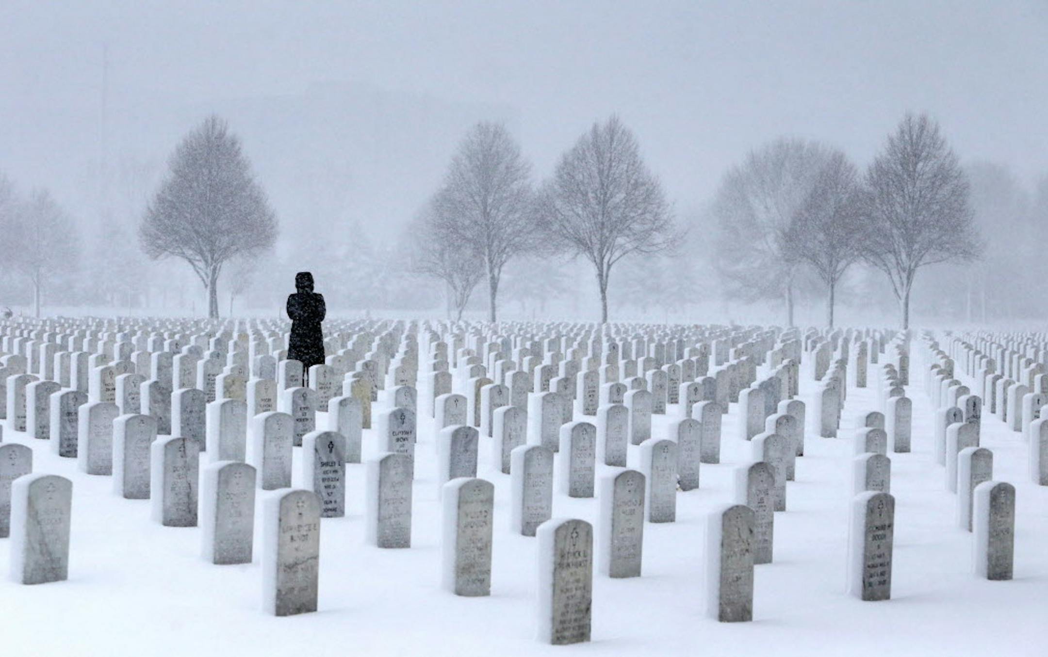 A woman visits a gravesite in the Fort Snelling National Cemetery in a snowstorm Wednesday, March 23, 2016, in Minneapolis, MN. ORG XMIT: MIN1603241220184195