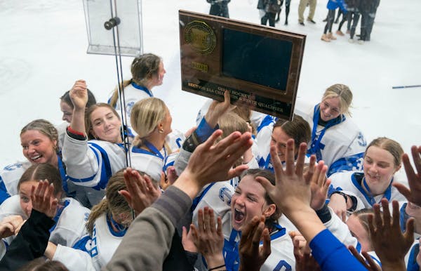 Minnetonka players rush the glass near the student section while forward Grace Sadura holds up their trophy after defeating Holy Family 4-0.