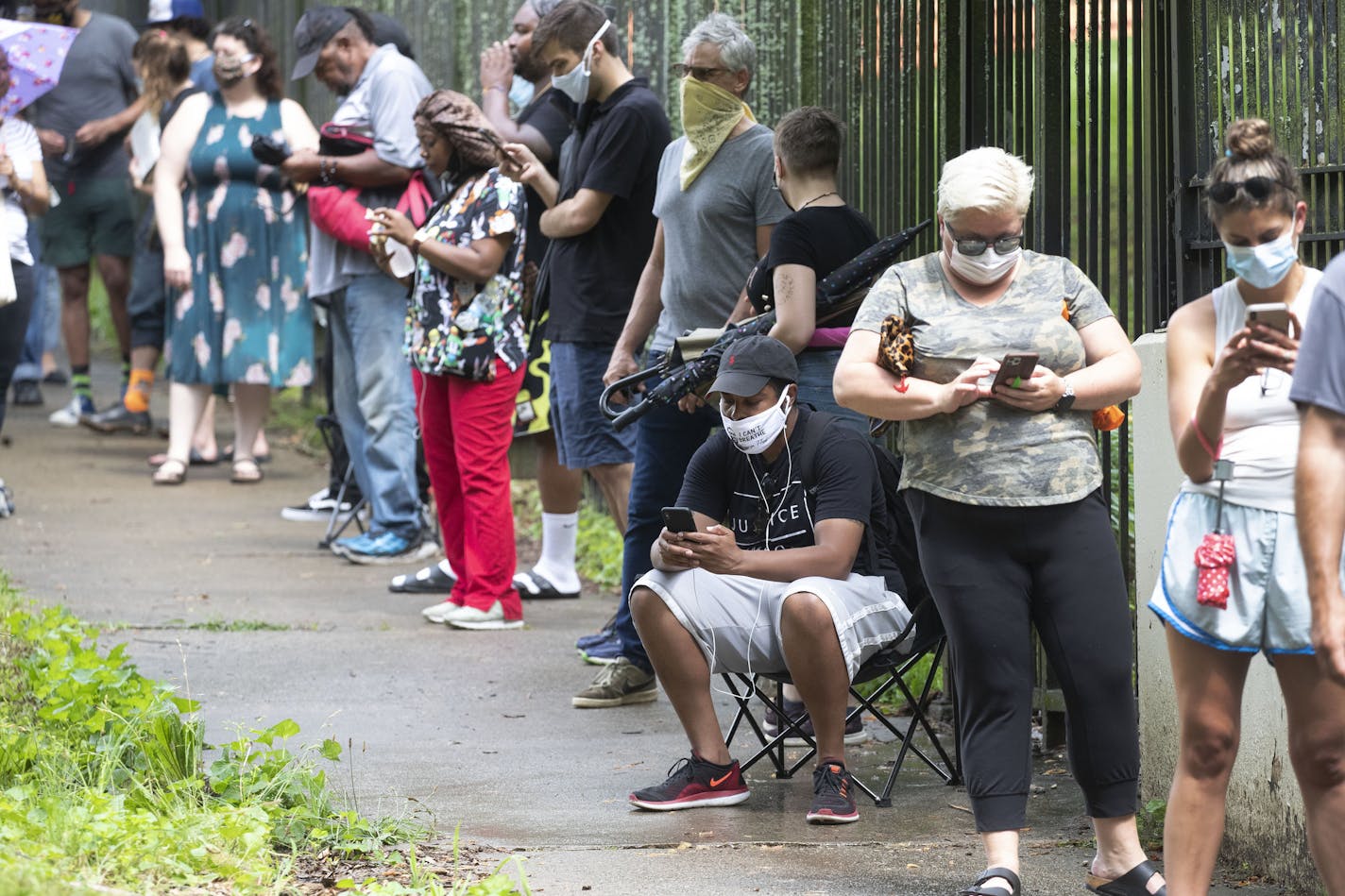 FILE - In this June 9, 2020, file photo, Steven Posey checks his phone as he waits in line to vote at Central Park in Atlanta. Voters reported wait times of three hours. When some Georgia voters endured a pandemic, pouring rain and massive waits earlier this month to cast their ballot, President Donald Trump and other Republicans blamed local Democrats for presiding over chaos. (AP Photo/John Bazemore, File)