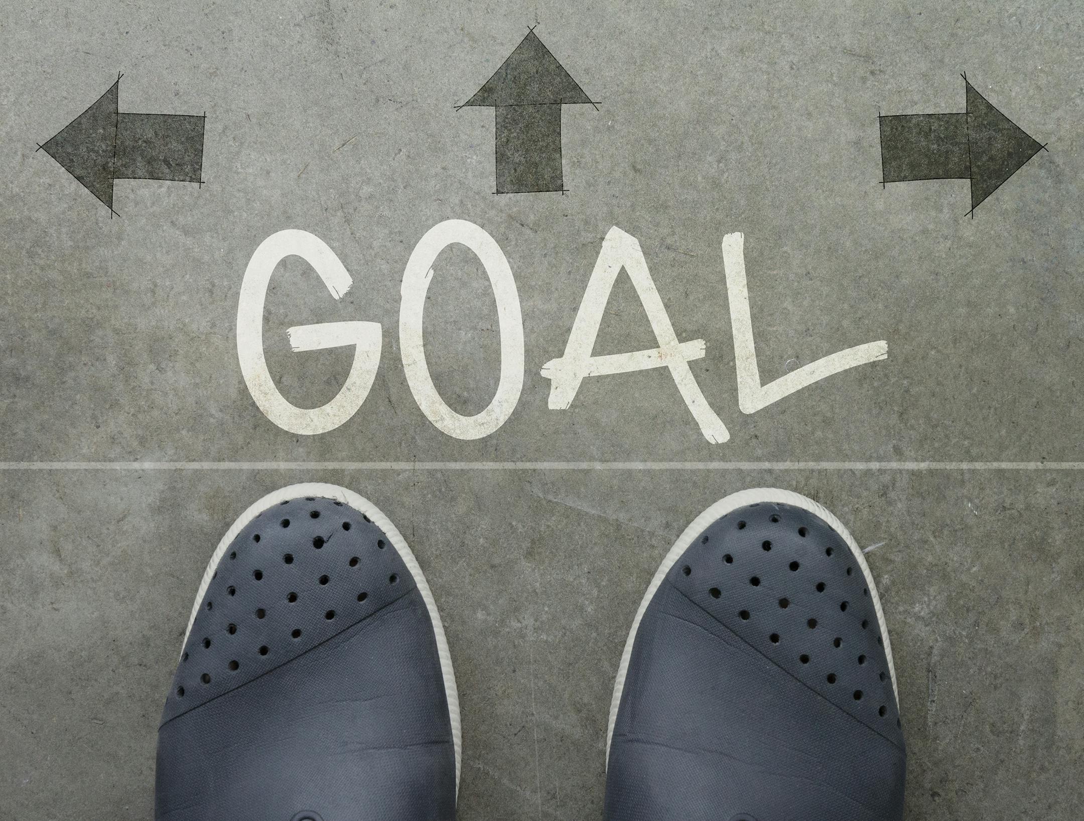 Hand drawn GOAL design word on front of business man feet as concept