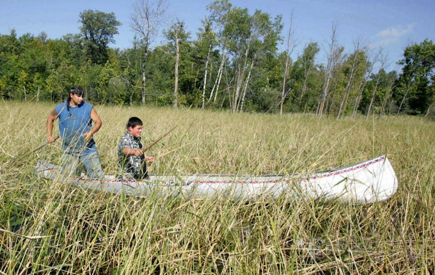 FILE - In this Aug. 30, 2006 file photo, Joe Hoagland, left, pushes a canoe through a wild rice bed in White Earth, Minn., as 14-year-old Chris Salazar learns how to harvest the rice by knocking the grain off the stalks with two sticks. The Minnesota Pollution Control Agency said Wednesday, March 12, 2014 that more data analysis must be done to determine whether it will recommend changes to the state's water quality standards to protect wild rice from sulfates. (AP Photo/Jim Mone, File) ORG XMIT