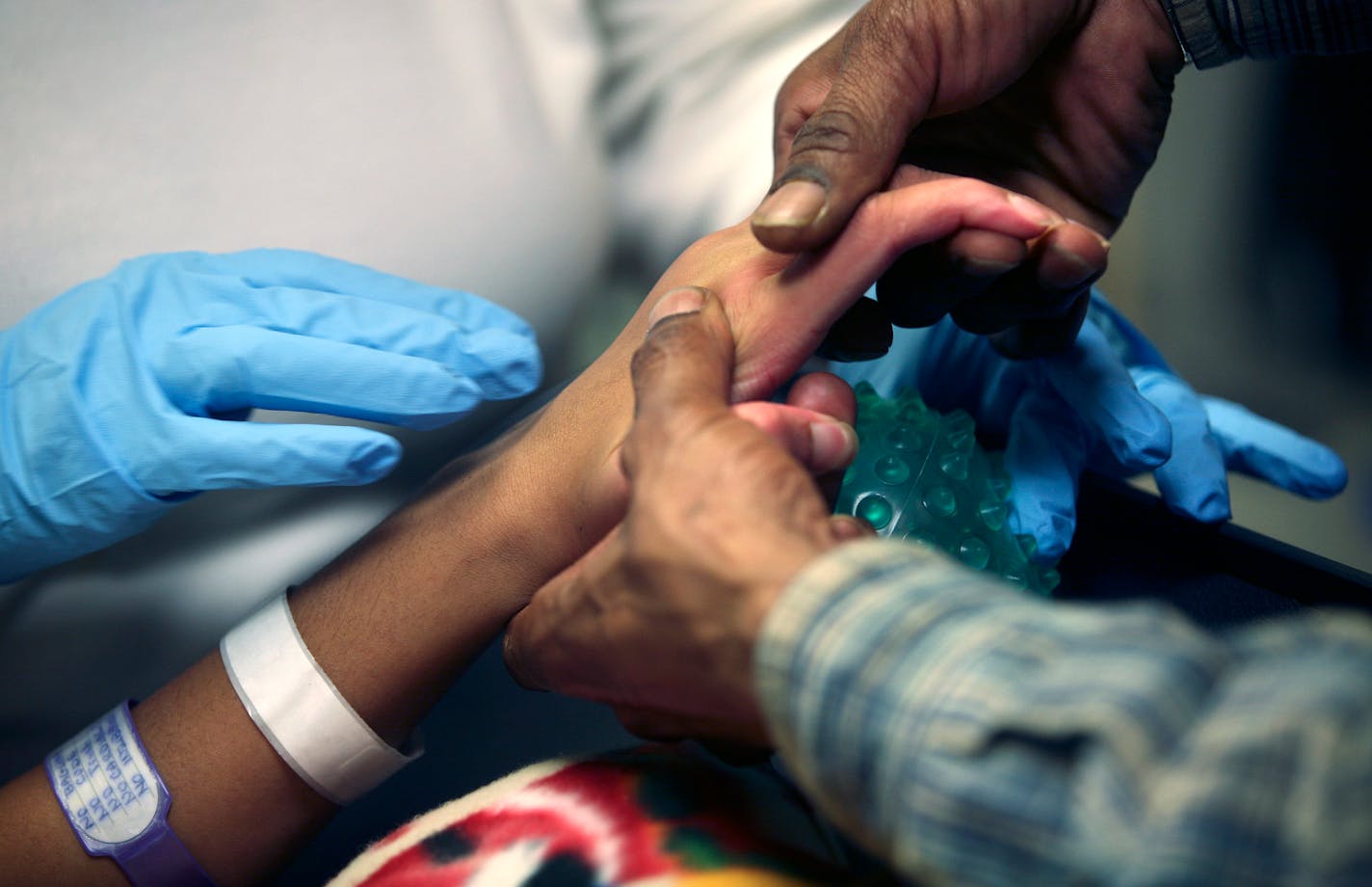 Steven Hall helped his daughter Vernice Hall reach out to grip a textured ball during a half-hour school session with teacher Debbie Zenker, blue gloves, at Gillette Children's Hospital. Twelve-year-old Vernice Hall was shot in the head two months ago. She recently had surgery to repair her skull and has started therapy at the hospital.