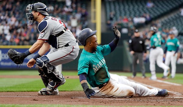 Seattle Mariners' Jean Segura, right, scores as Twins catcher Mitch Garver waits for the throw during the first inning
