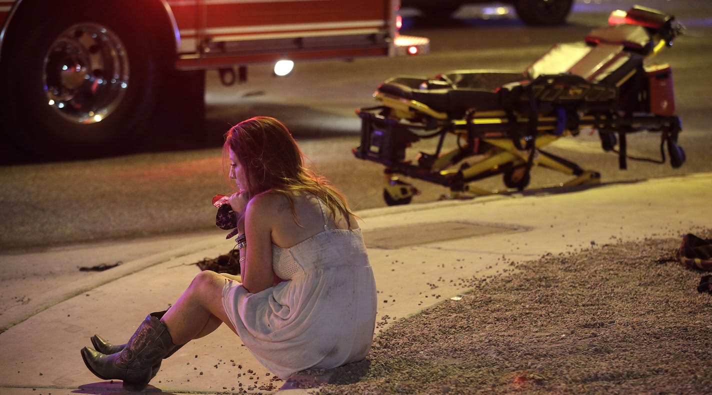 A woman sits on a curb at the scene of a shooting outside of a music festival along the Las Vegas Strip, Monday, Oct. 2, 2017, in Las Vegas. Multiple victims were being transported to hospitals after a shooting late Sunday at a music festival on the Las Vegas Strip. (AP Photo/John Locher) ORG XMIT: MIN2017100205102104