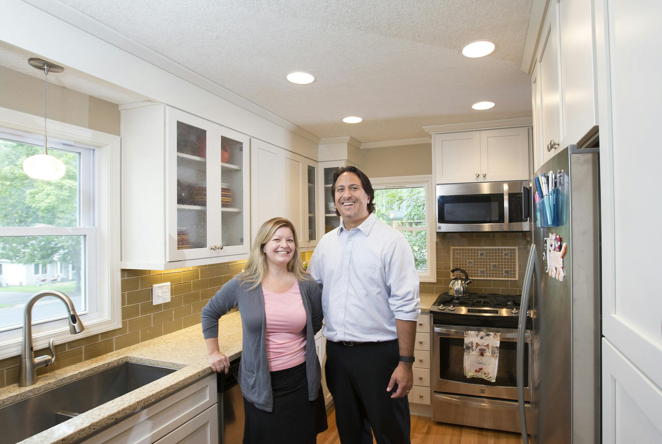 Theresa Schneider and Mark Simpson in their revitalized kitchen, which features a mix of earth-tone accents, stainless steel and crisp white woodwork.