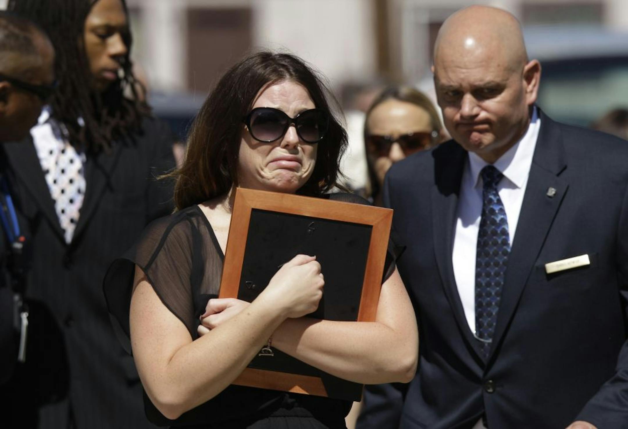 A woman carrying a frame is escorted from where the family of Aurora, Colo., movie theater shooting victim Micayla Medek had gathered before Medek's funeral to the church Thursday, July 26, 2012, in Denver.