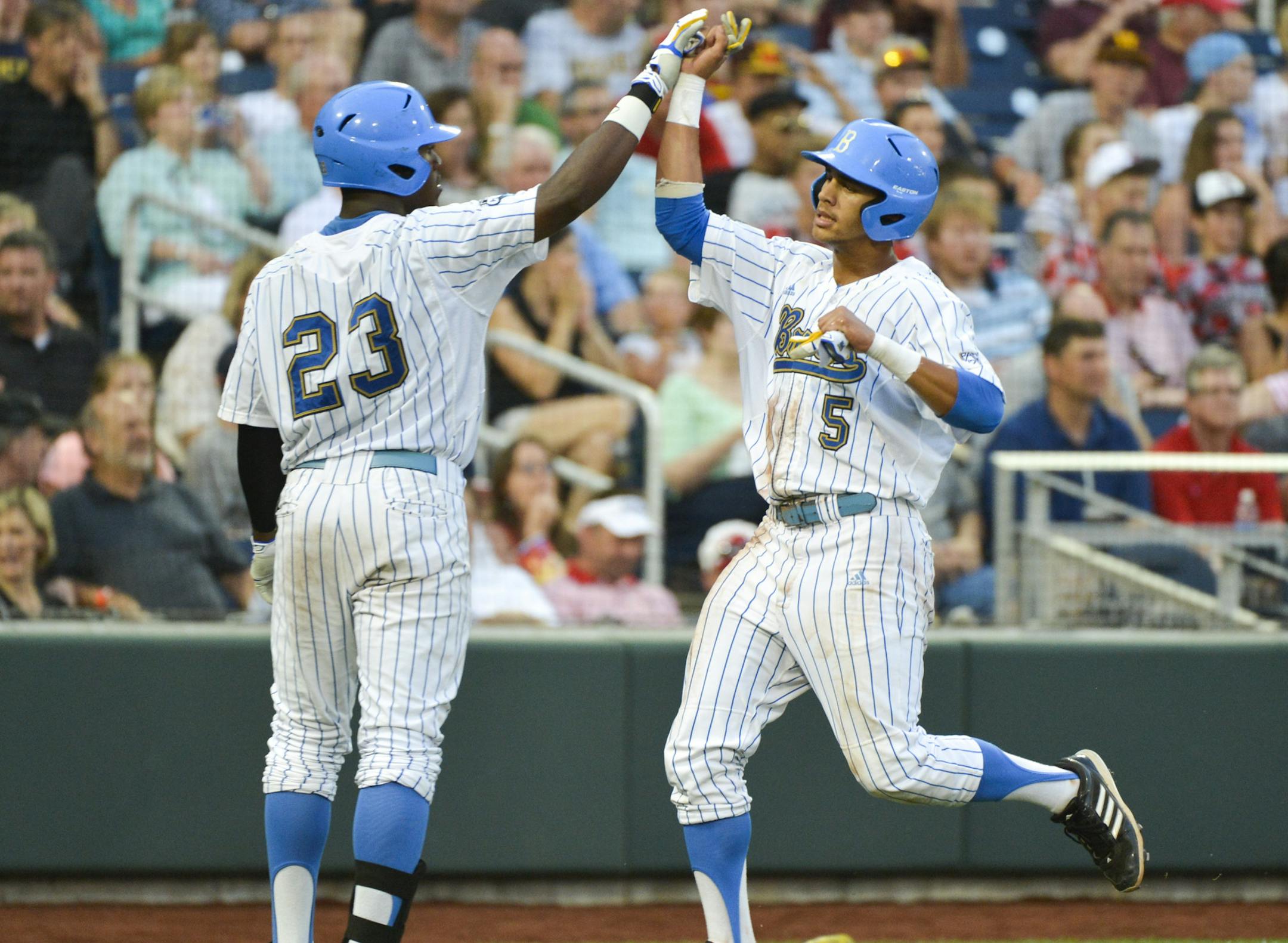 UCLA's Kevin Williams (5) is greeted by Brenton Allen (23) after he scored against Mississippi State on a single by Cody Regis in the fourth inning of Game 2 in their NCAA College World Series baseball finals, Tuesday, June 25, 2013, in Omaha, Neb. (AP Photo/Ted Kirk)